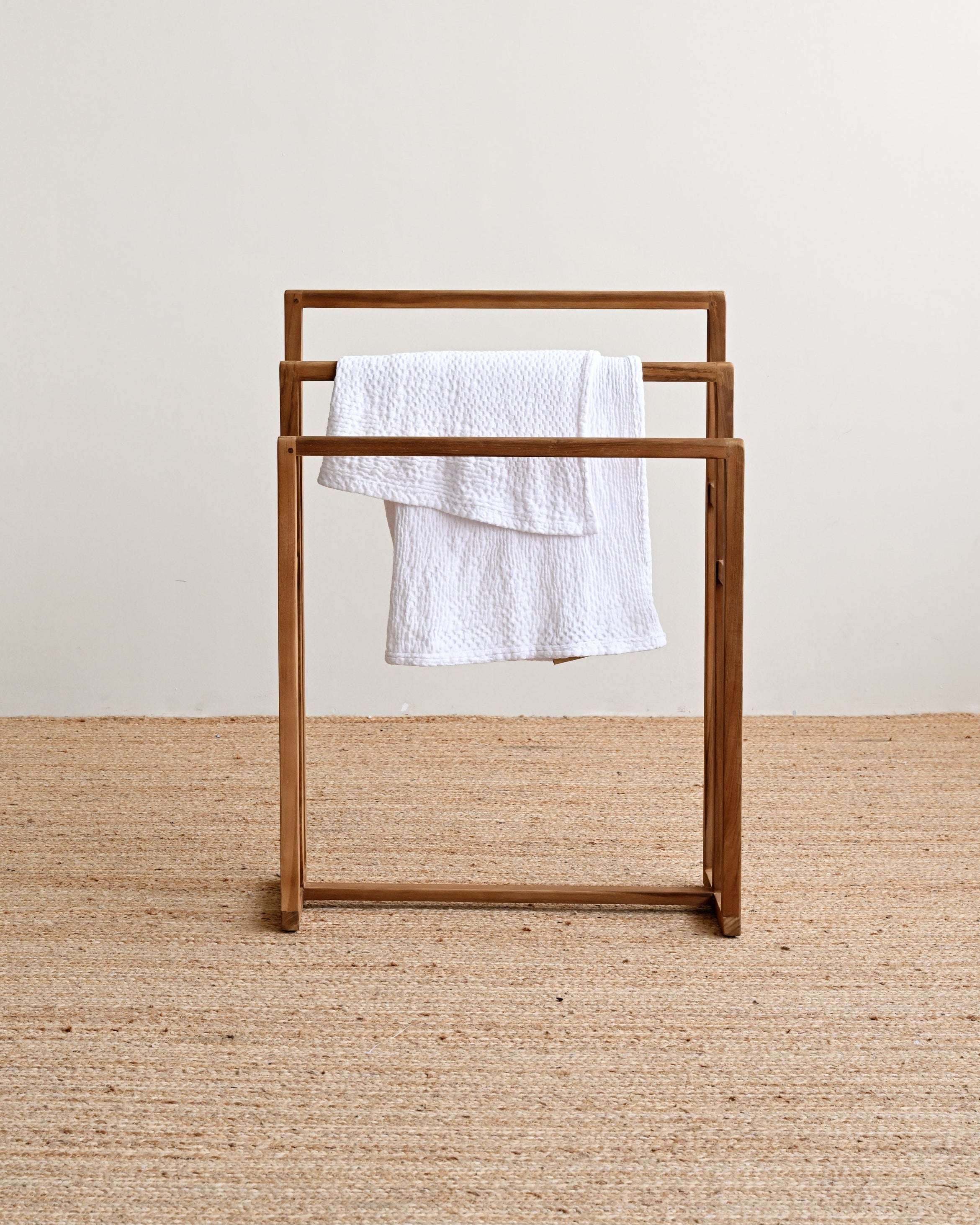 Wooden towel rack with a white towel on a beige carpet and light-colored wall background