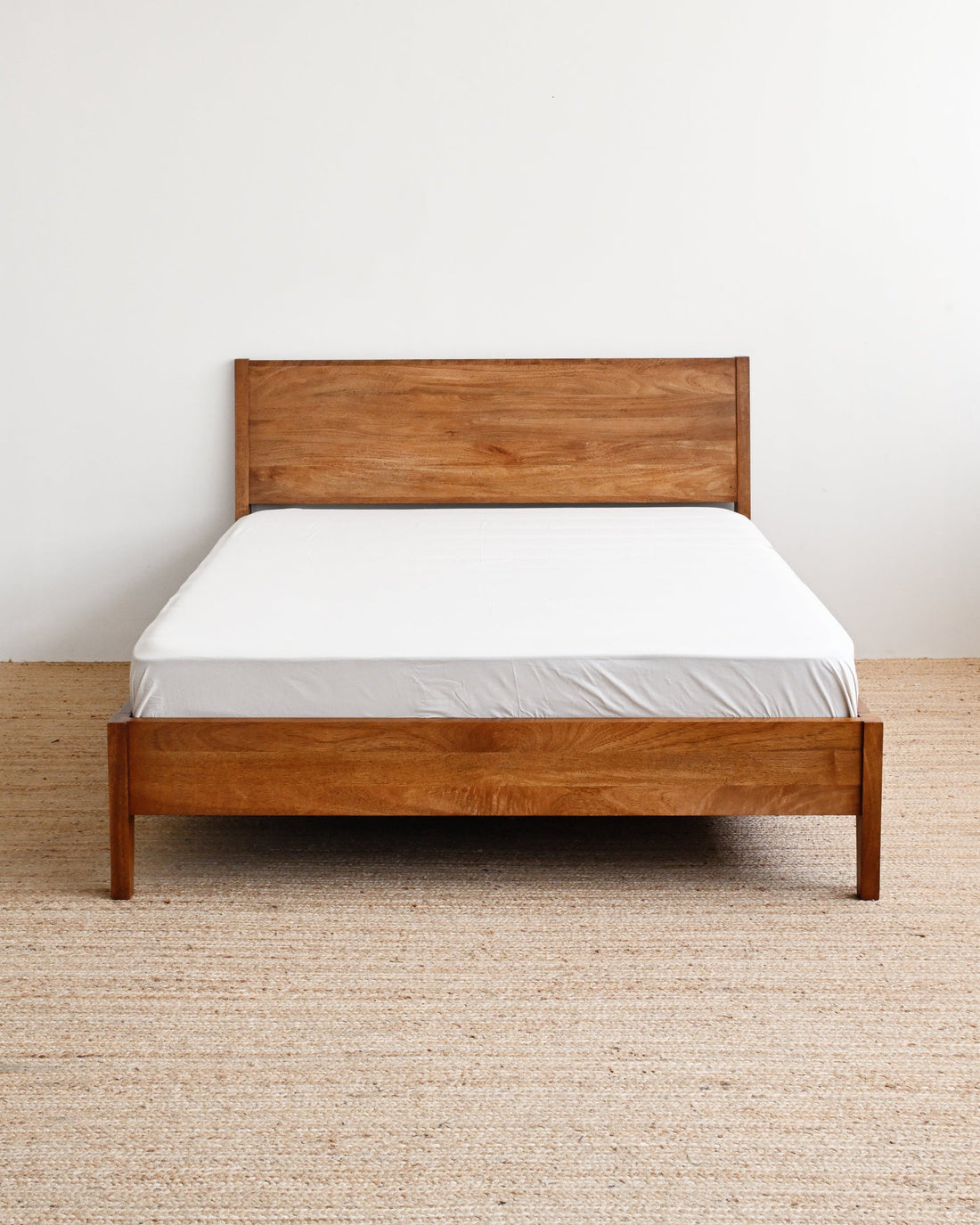 Wooden bed with white mattress against a plain wall
