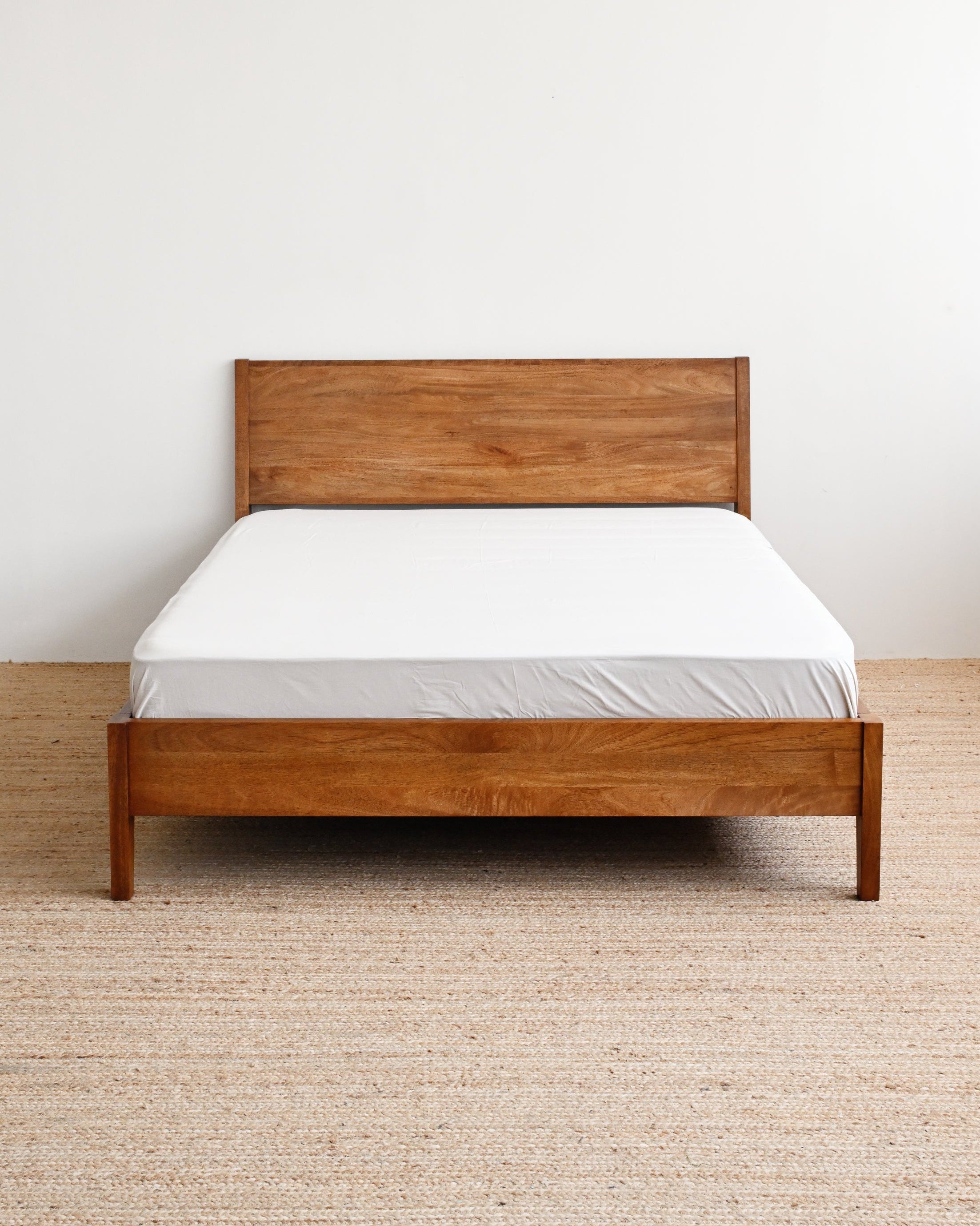 Wooden bed with white mattress against a plain wall