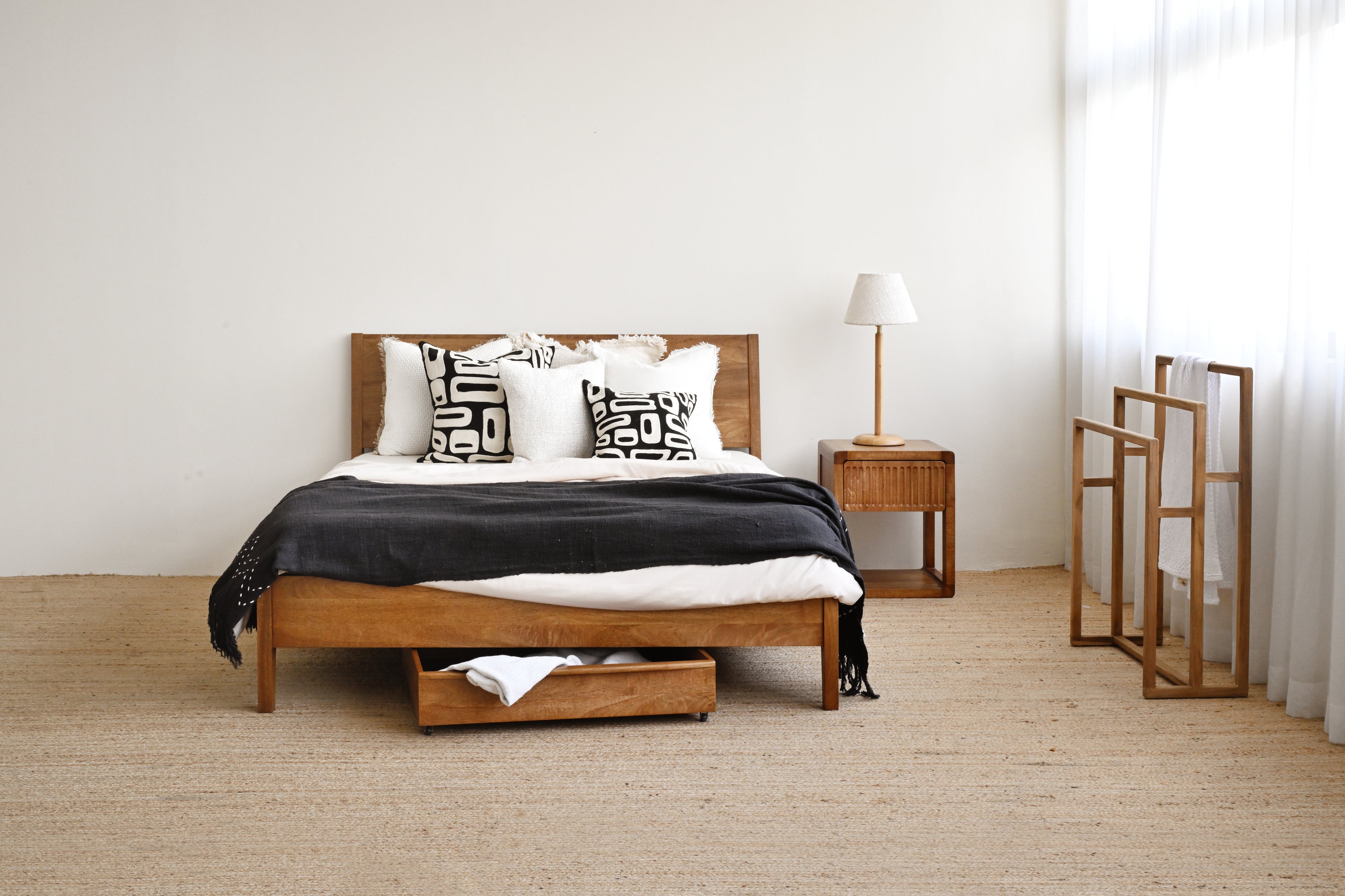 Wooden bed with storage drawers in a minimalistic bedroom setting.