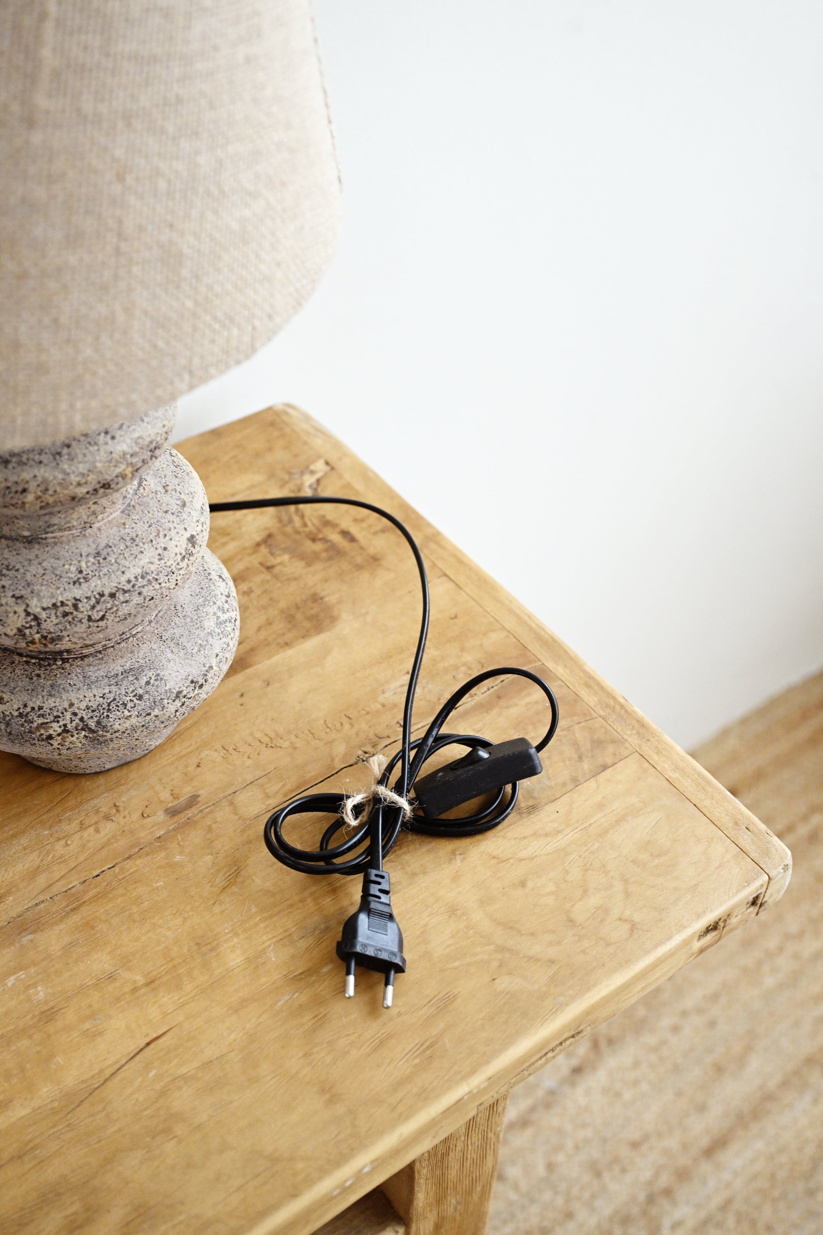 Table lamp with a beige shade and stone base on a wooden surface, with a black power cord.