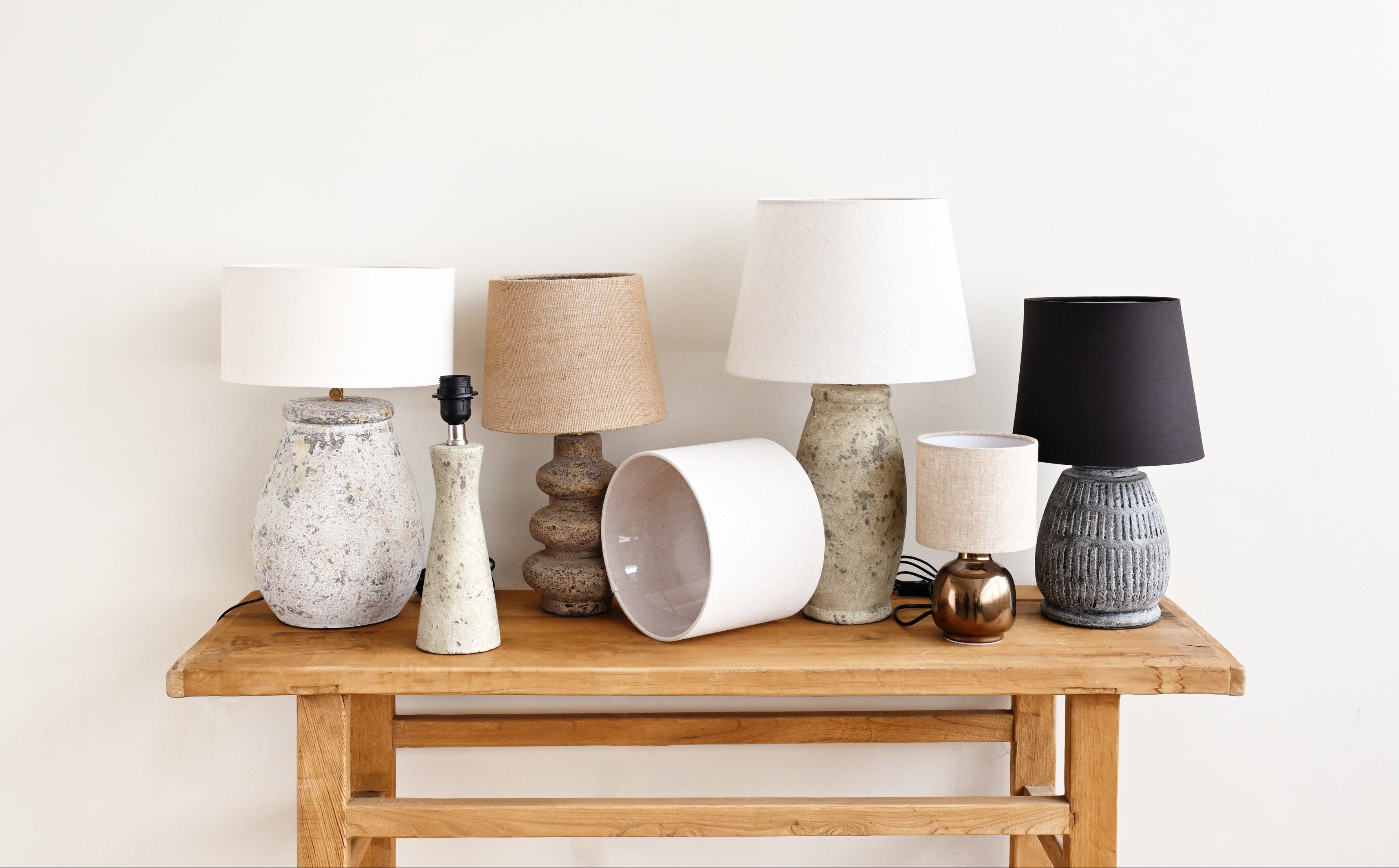 Collection of various lamps on a wooden table against a white wall