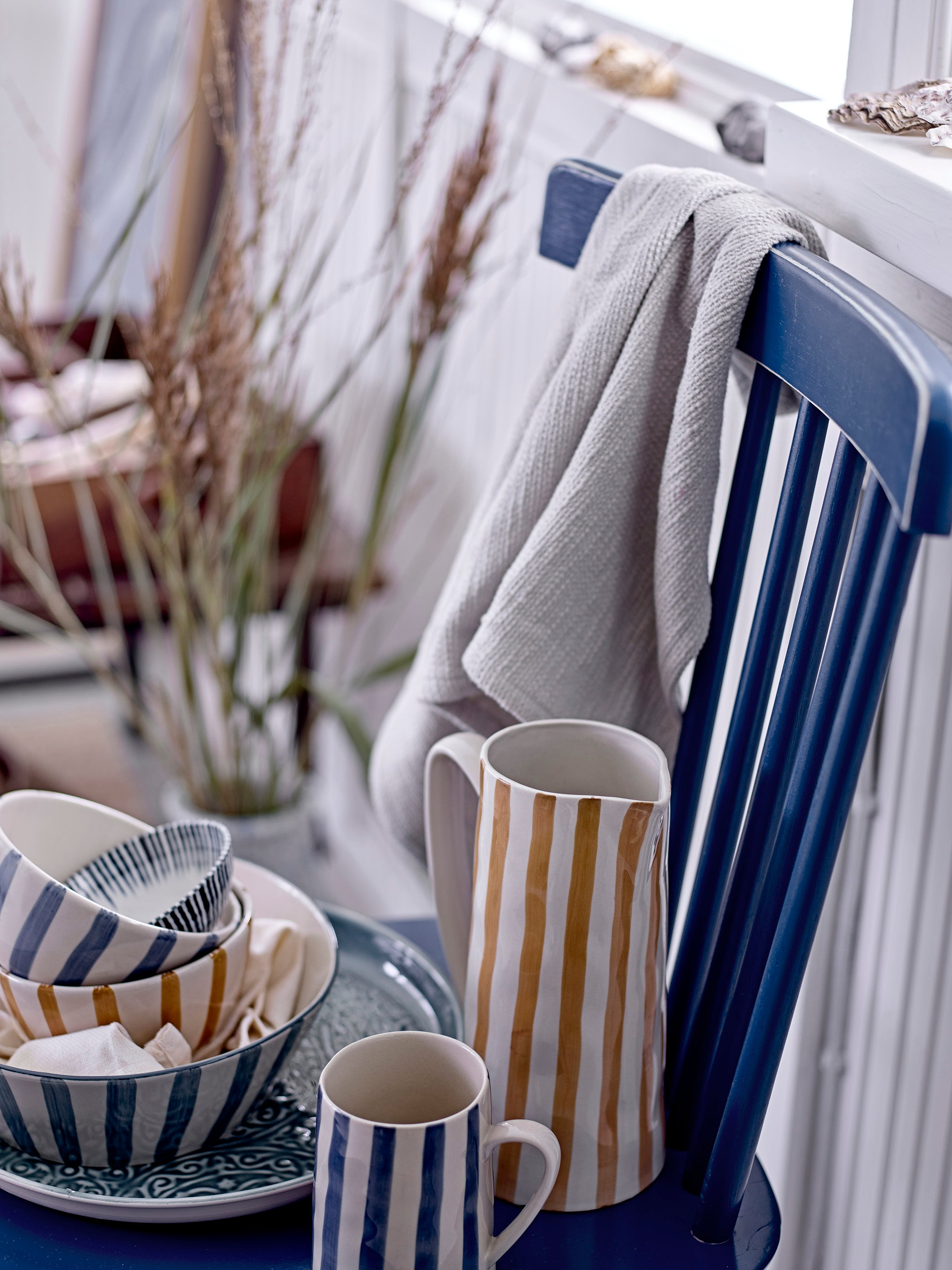 Striped ceramic items on a table with a chair and plant in the background