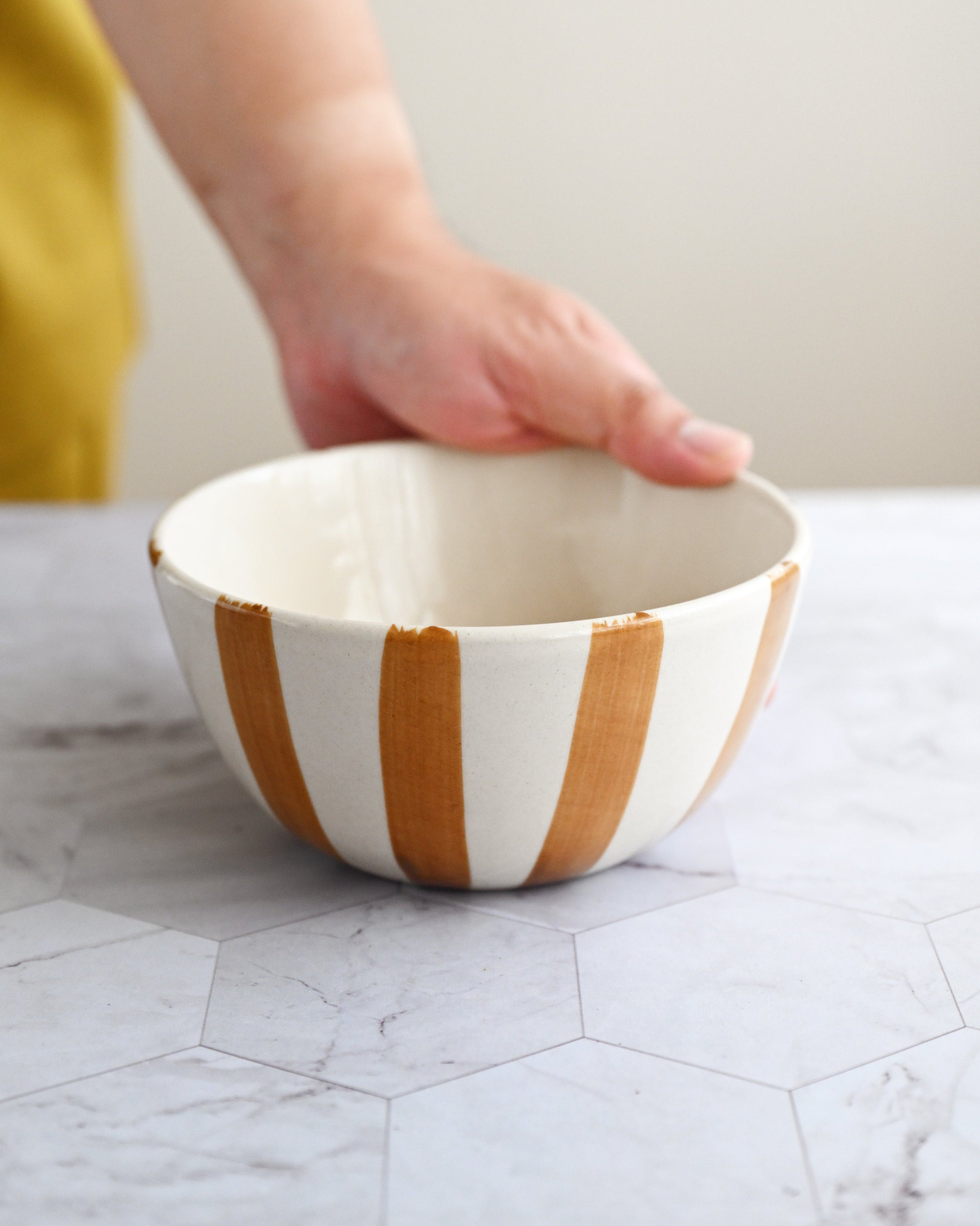 Hand holding a ceramic bowl with brown and white stripes on a marble surface.