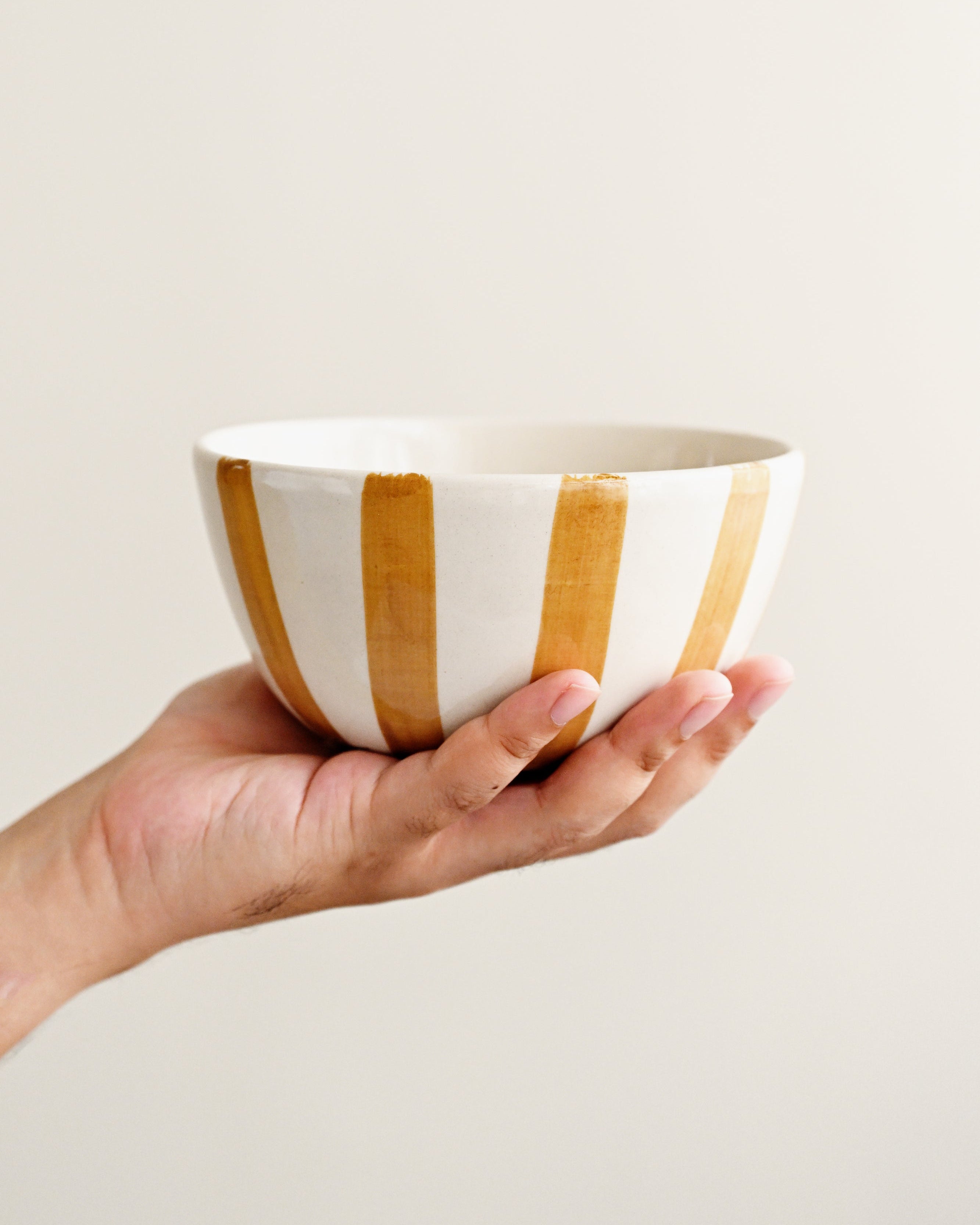 Hand holding a ceramic bowl with gold stripes against a plain background