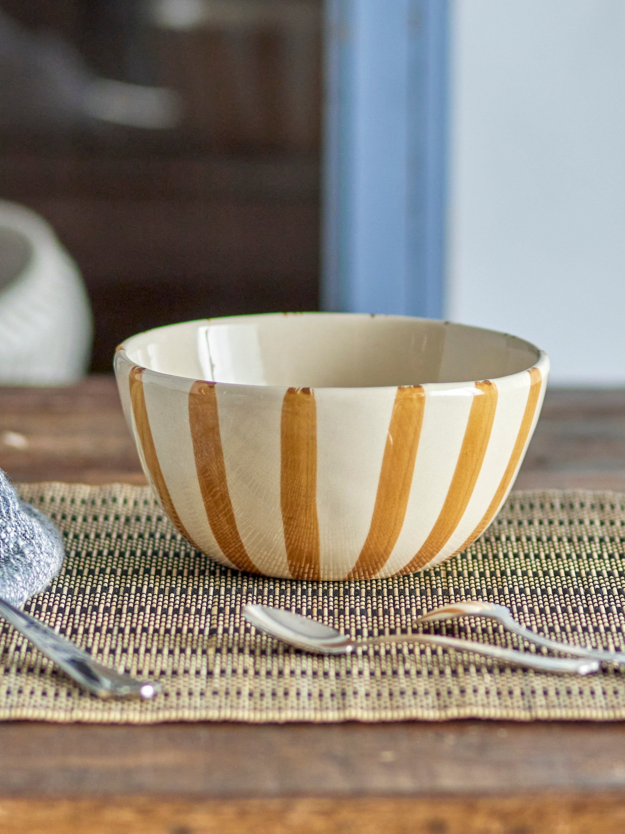 Wooden bowl with gold stripes on a woven placemat with cutlery