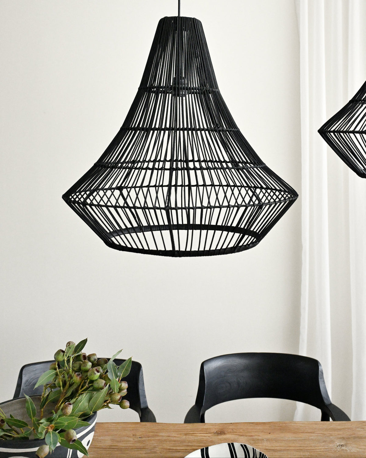 Black woven pendant light fixture hanging above a dining table with chairs.