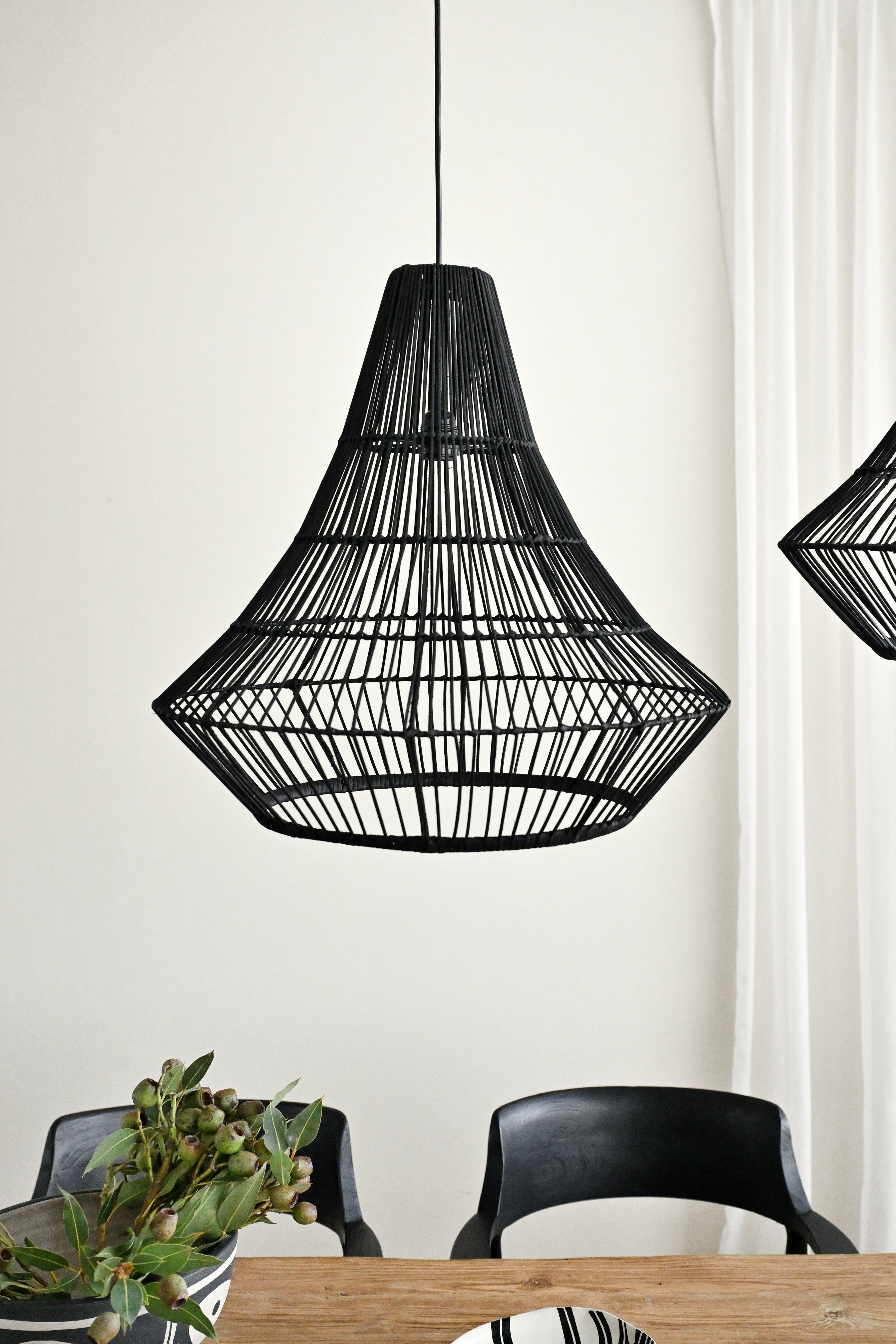 Black woven pendant light fixture hanging above a dining table with chairs.