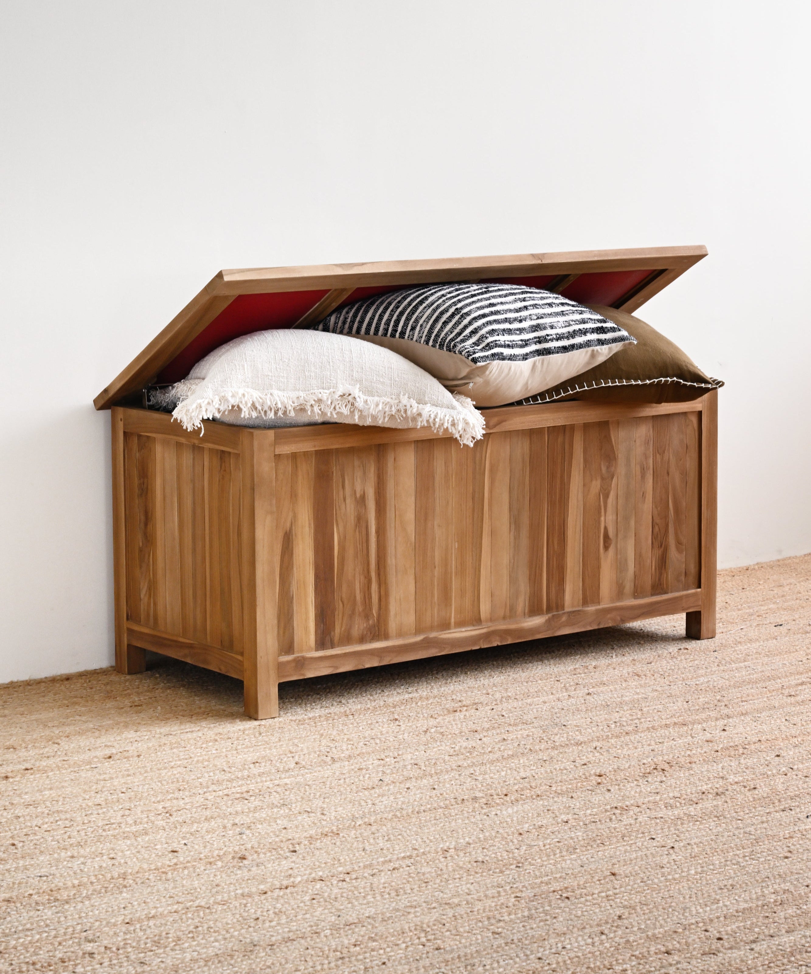 Wooden storage chest with pillows on a carpeted floor against a white wall