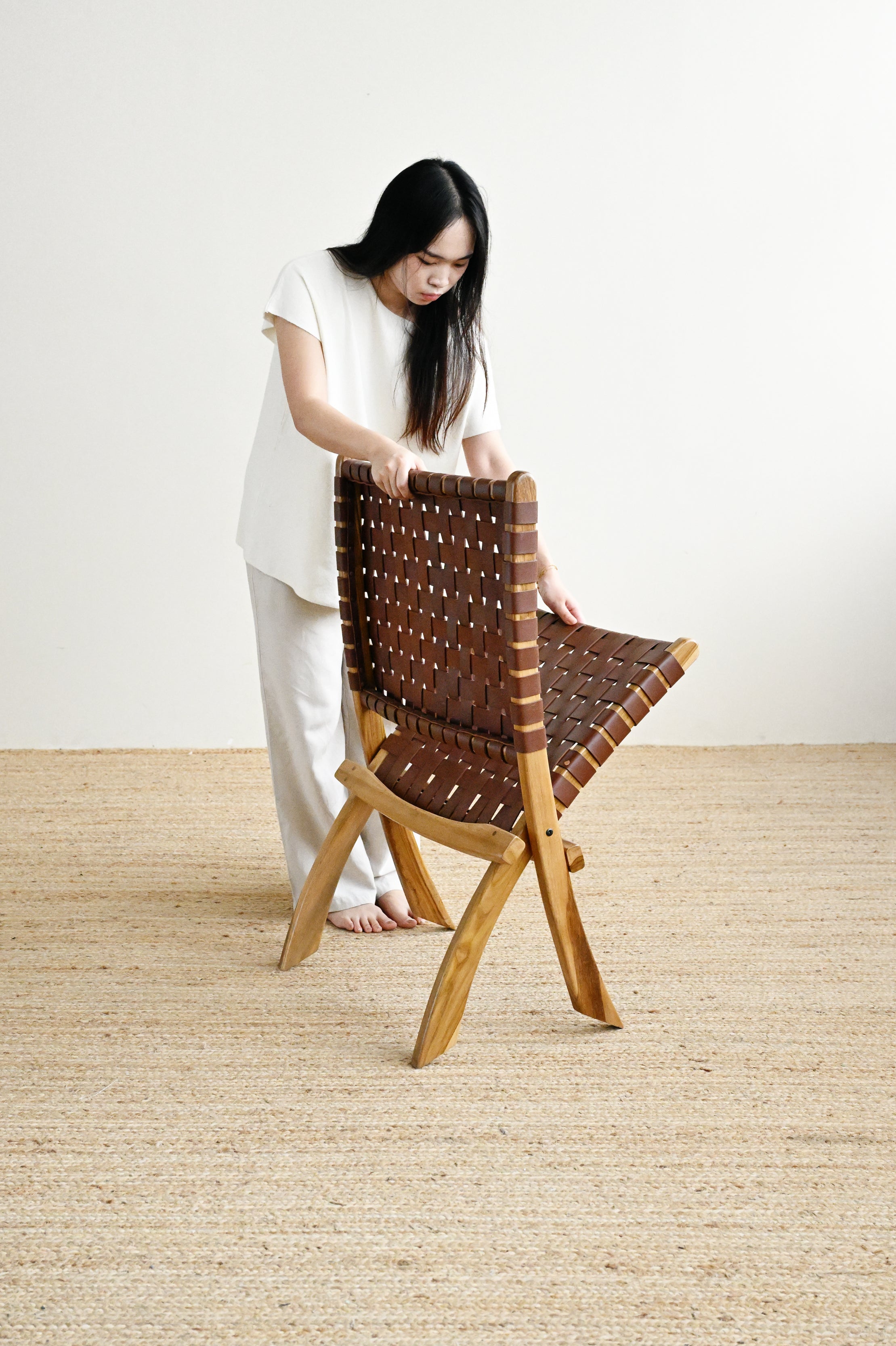 Woman standing next to a woven chair on a plain floor.