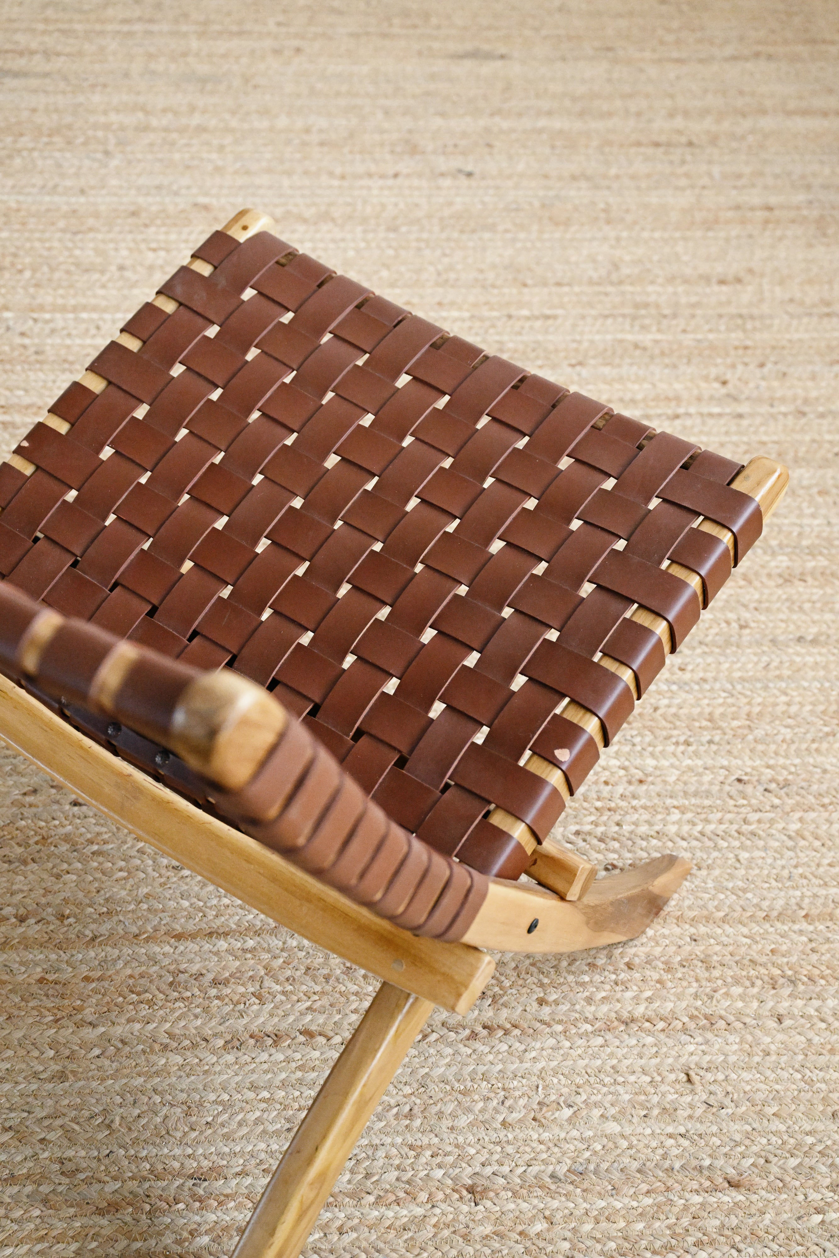 Brown woven stool with wooden legs on a beige textured background