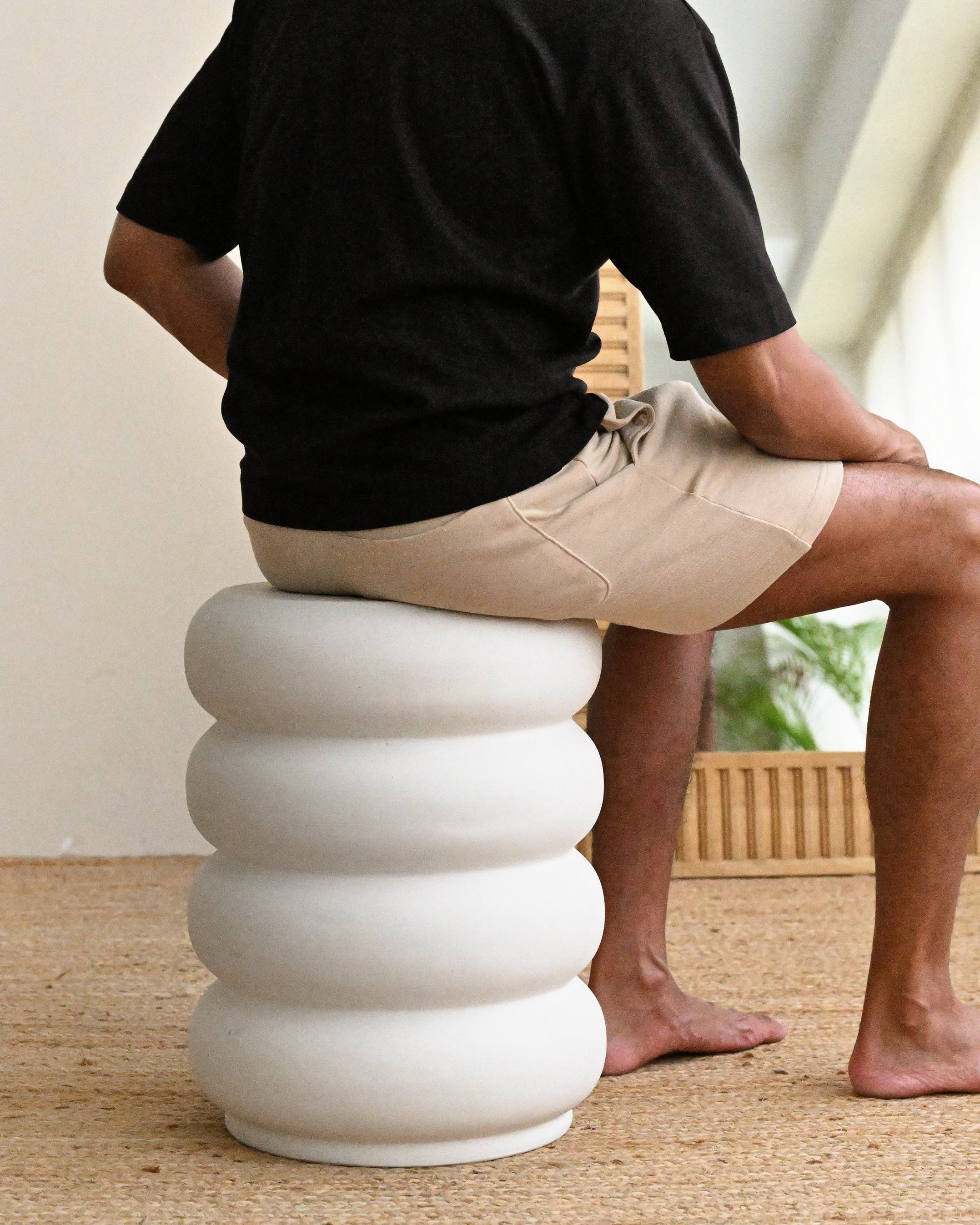 Person sitting on a white, ribbed stool in a room with a mirror and beige walls.