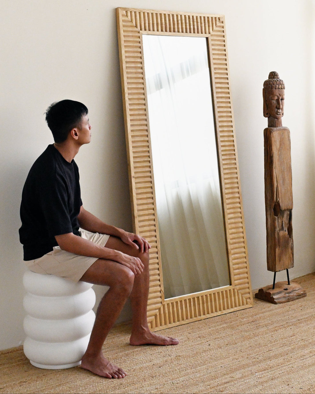 Person sitting on a white cushion in front of a large mirror with a wicker frame.