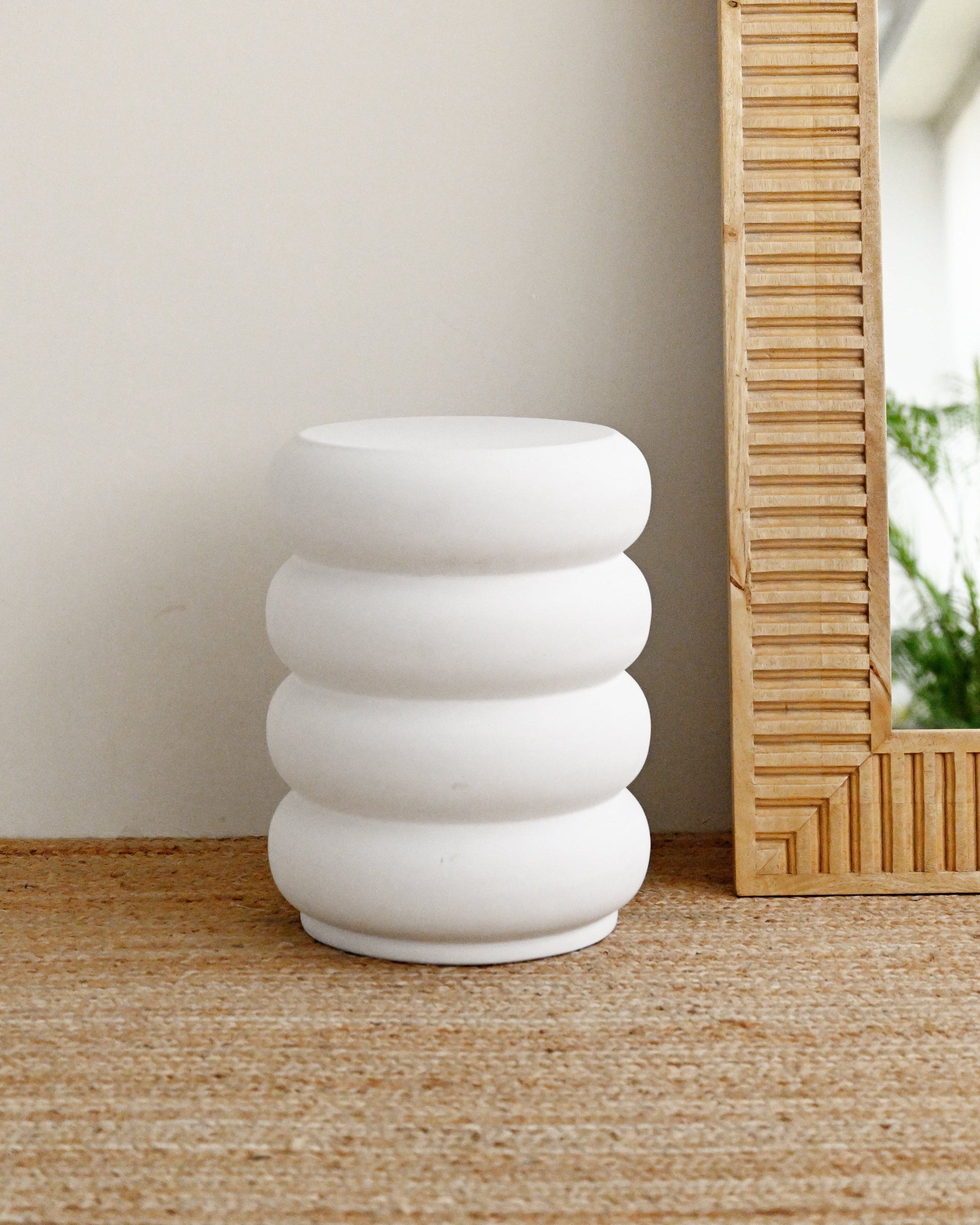 White concrete stool with stacked rings on a wooden floor next to a mirror.