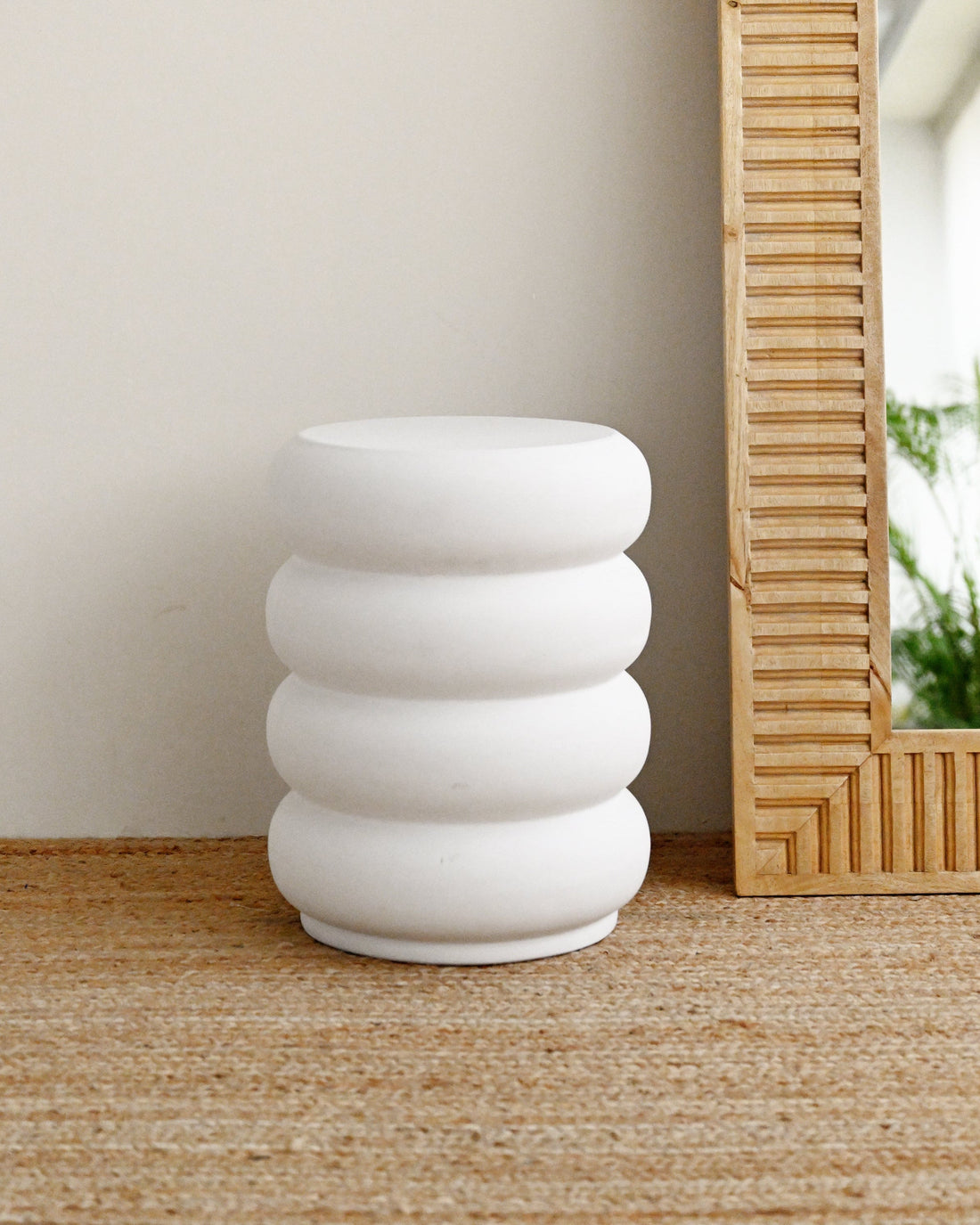 White concrete stool with stacked rings on a wooden floor next to a mirror.