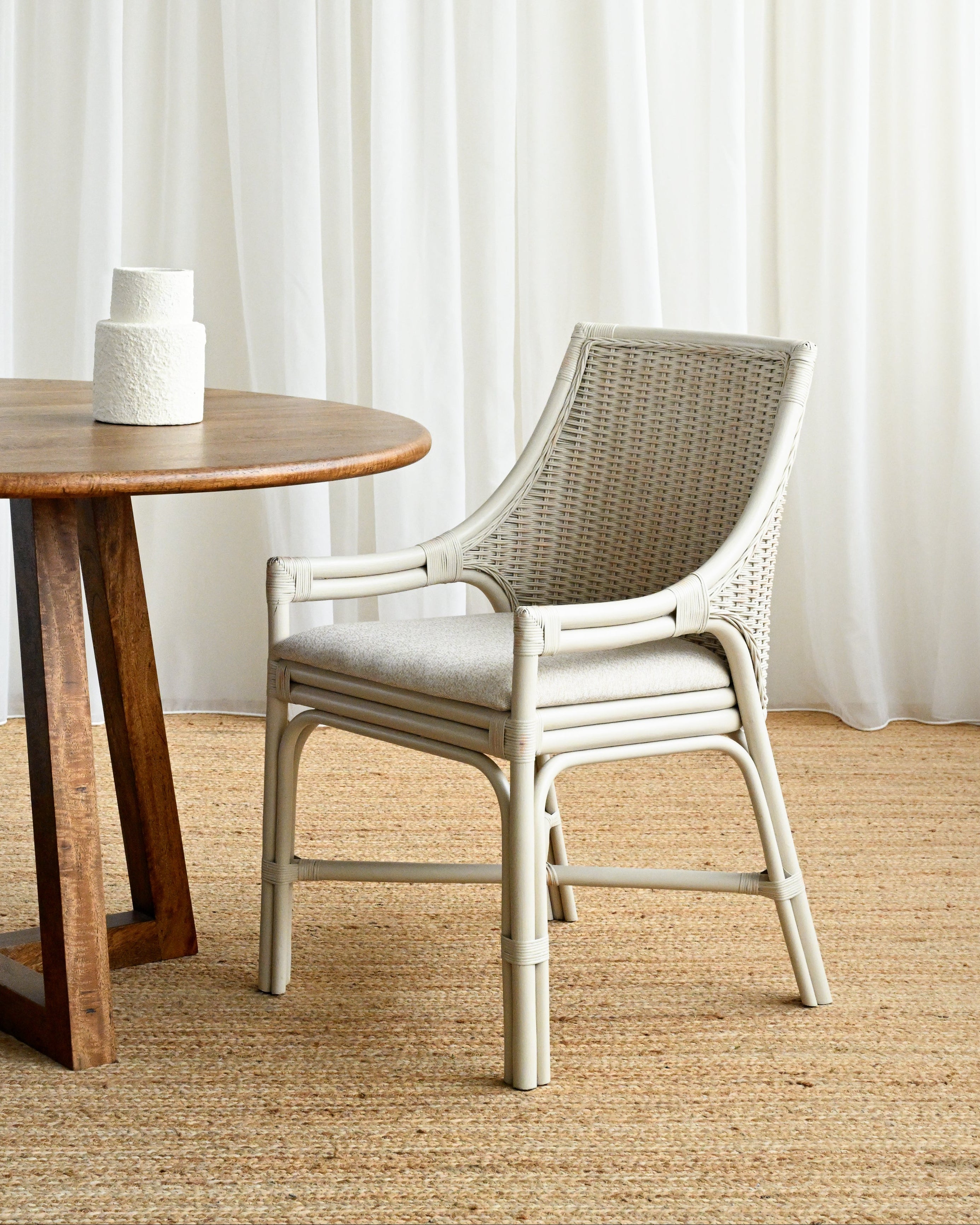 Wicker chair next to a wooden table with white curtains in the background