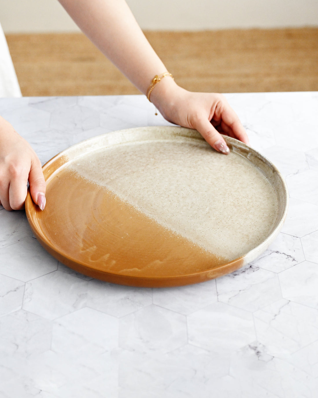 Person holding a ceramic plate with a gradient design on a marble surface.