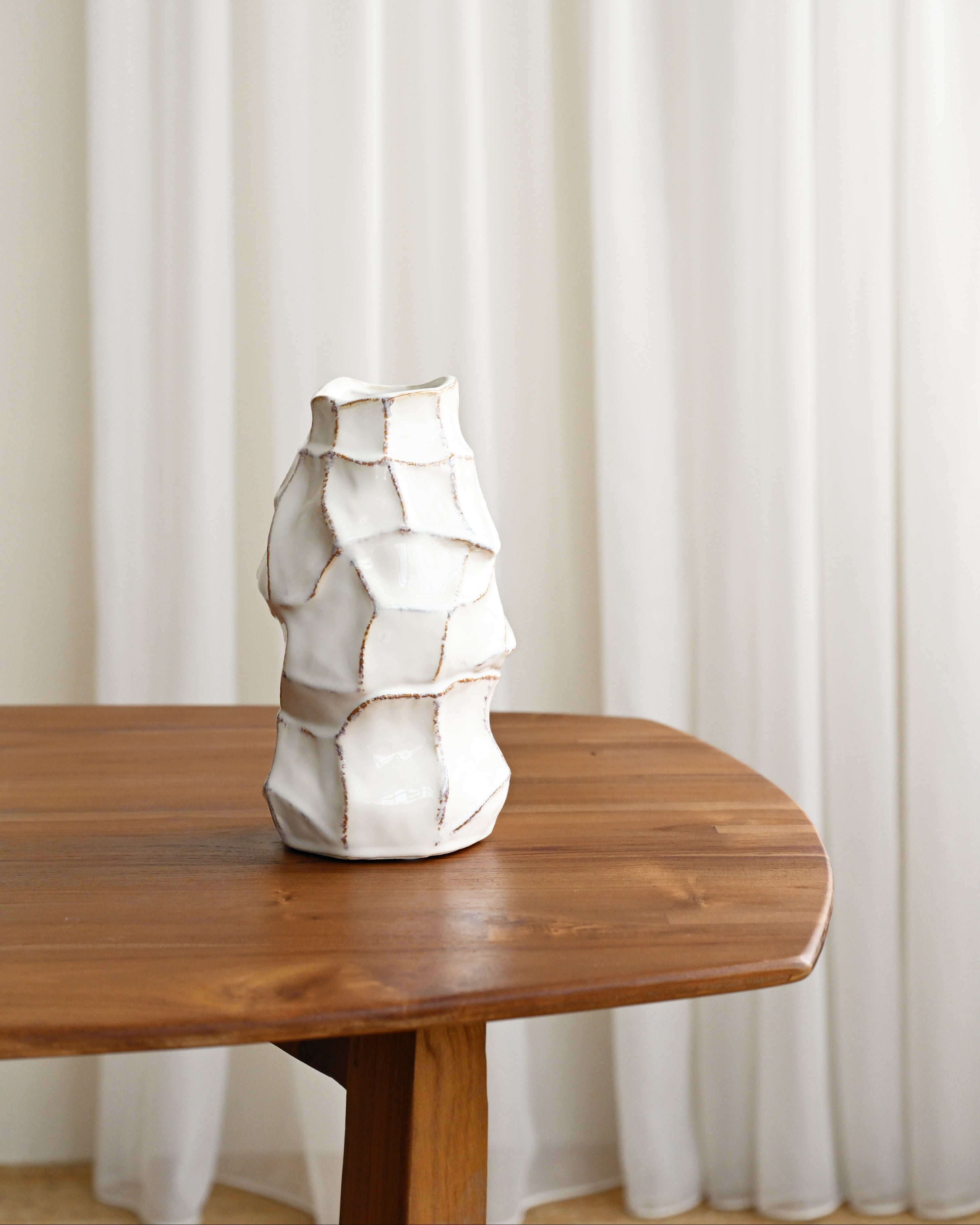 White ceramic vase on a wooden table with white curtains in the background