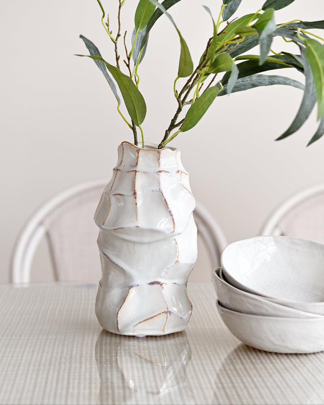 White ceramic vase with wavy texture holding green leaves on a light surface.