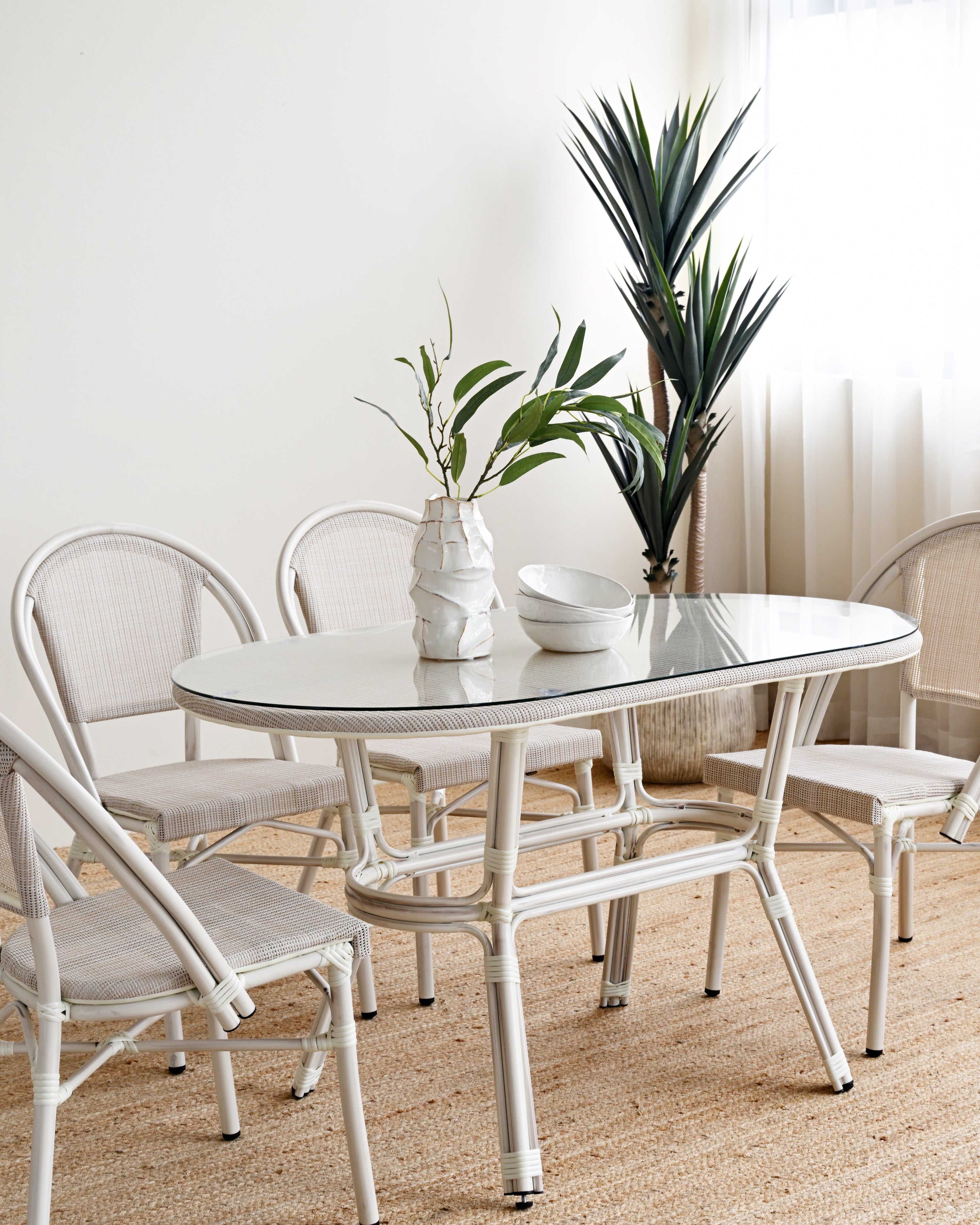 White dining set with table and chairs in a room with plants and curtains.