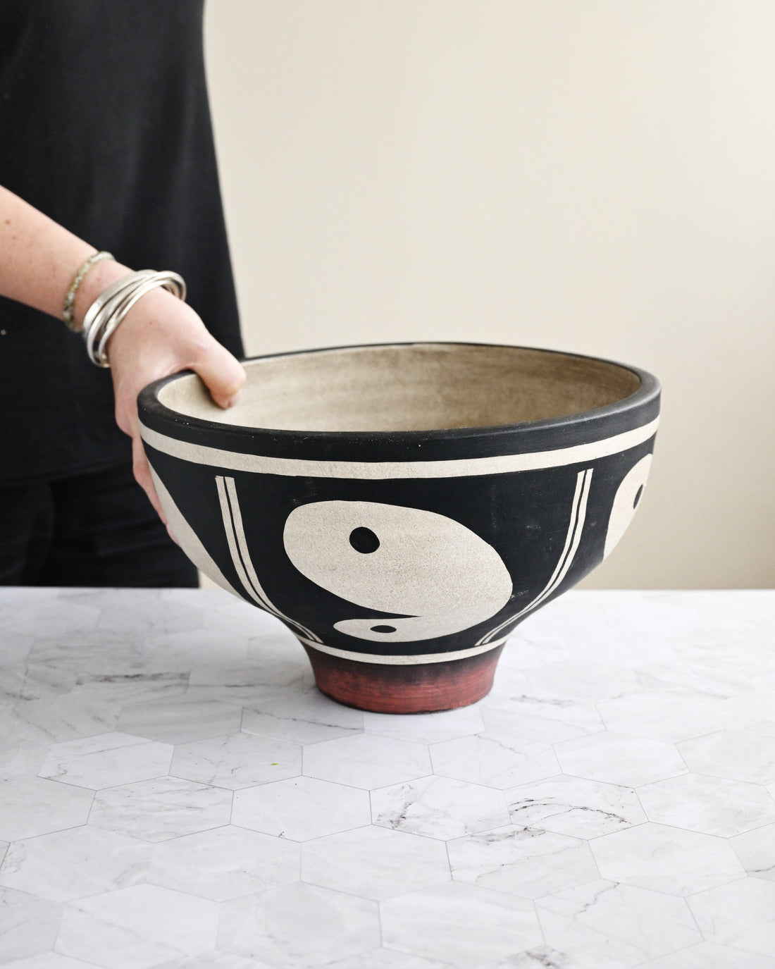Ceramic bowl with yin yang design held by a person on a marble surface