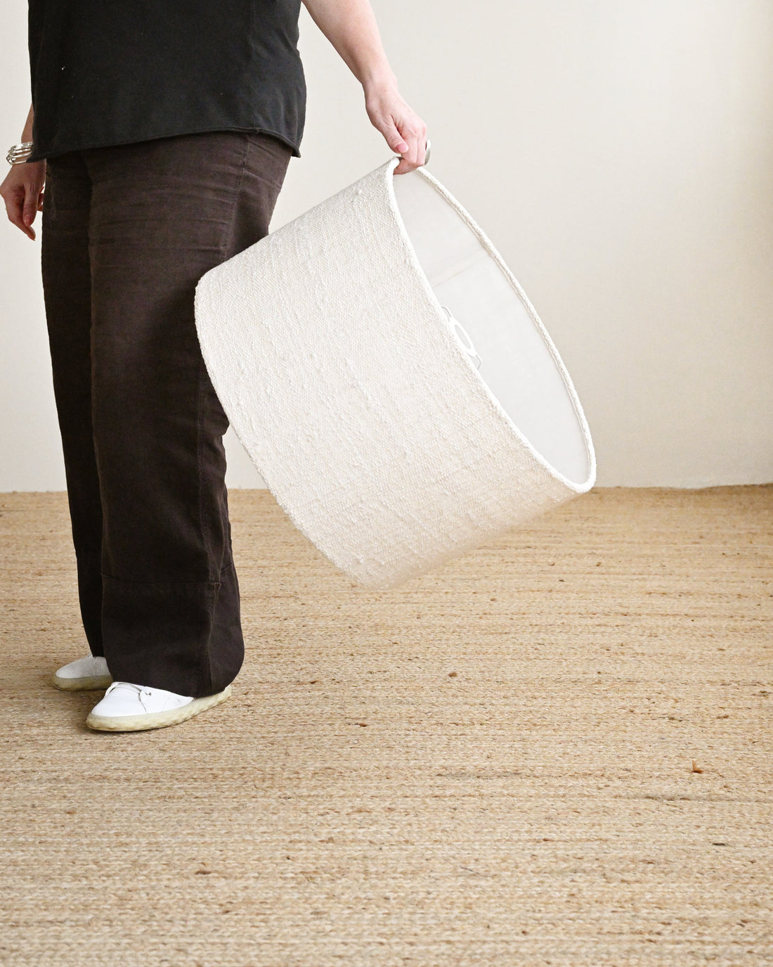 A person holding a white lampshade in a room with a plain wall.