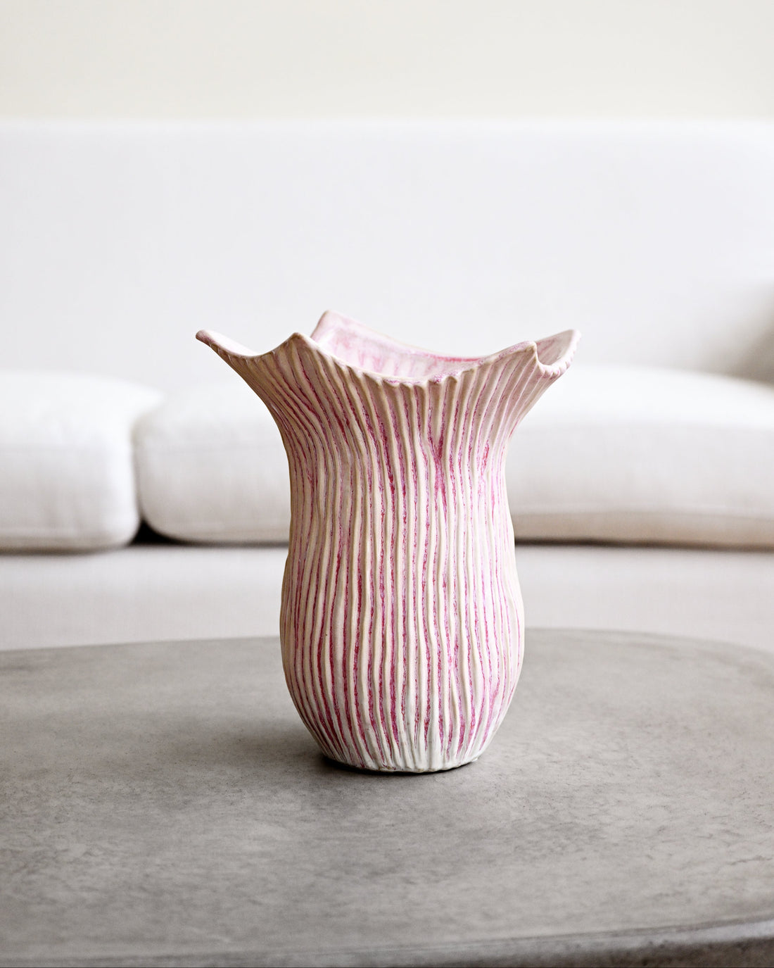 Pink and white striped vase on a gray surface with a blurred white background