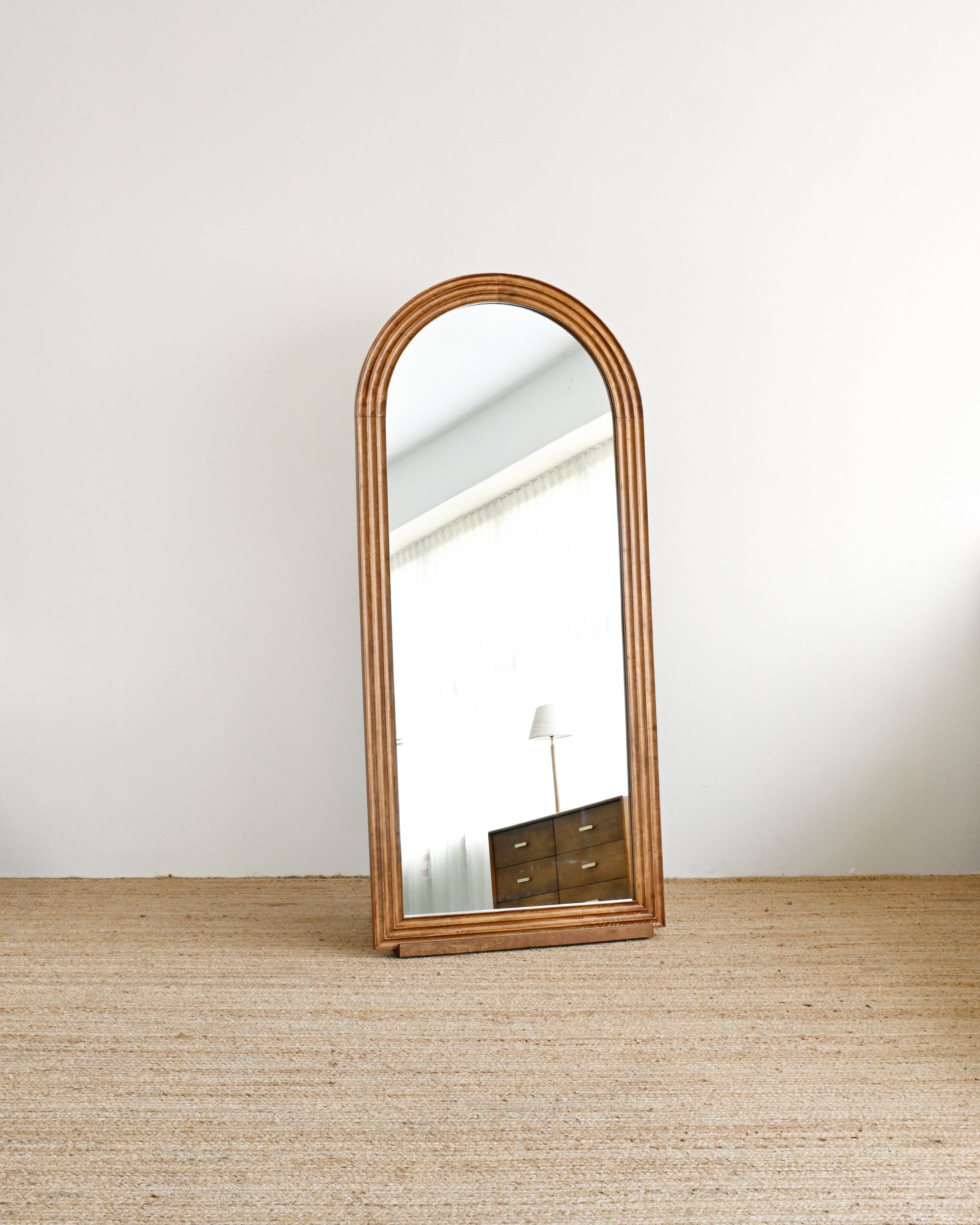 Wooden floor mirror leaning against a white wall on a wooden floor.