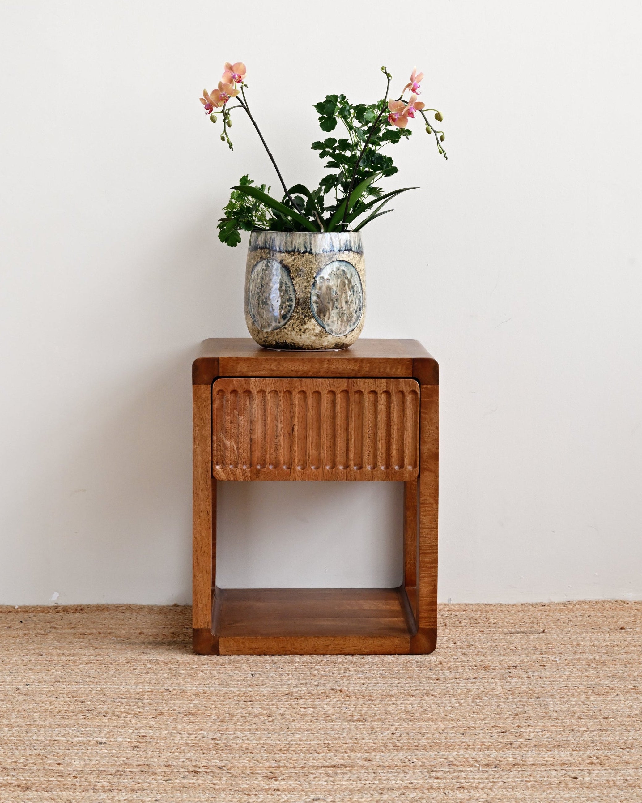 Wooden side table with a vase of flowers on a beige carpet