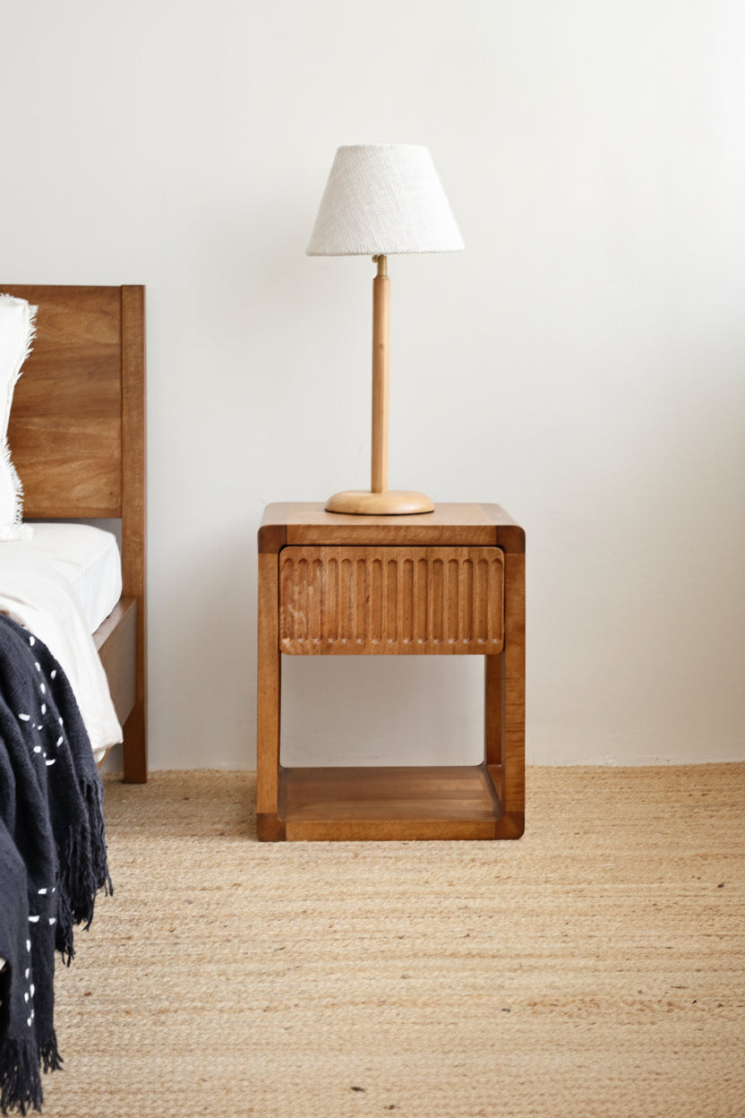Wooden nightstand with lamp next to a bed in a bedroom setting