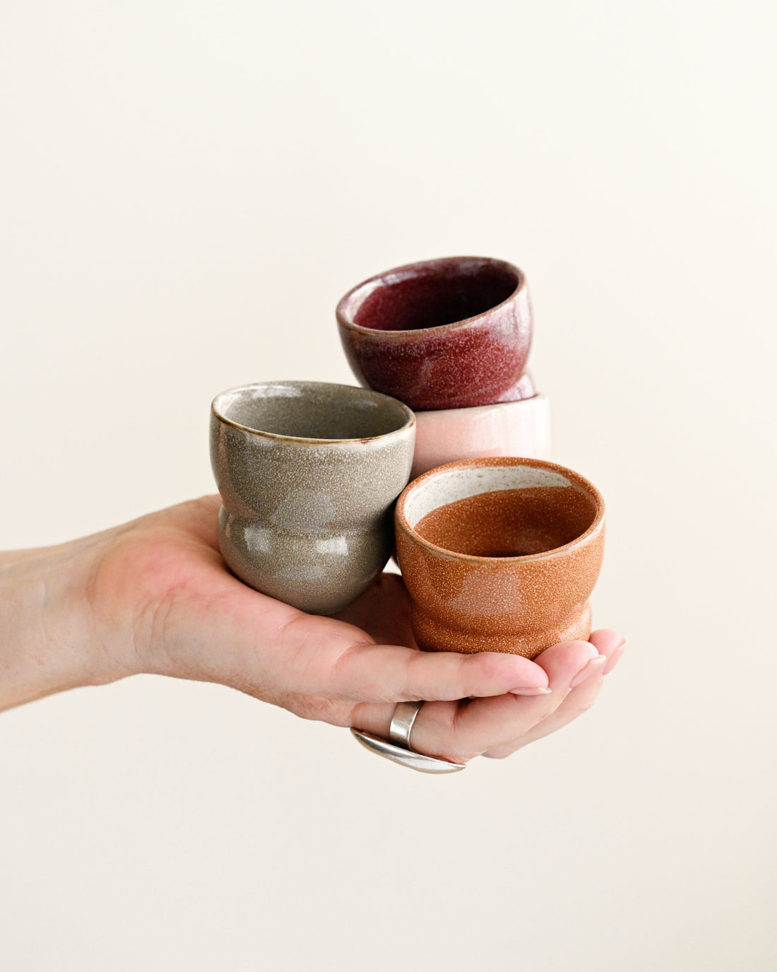 Three small ceramic cups held in a hand against a plain background