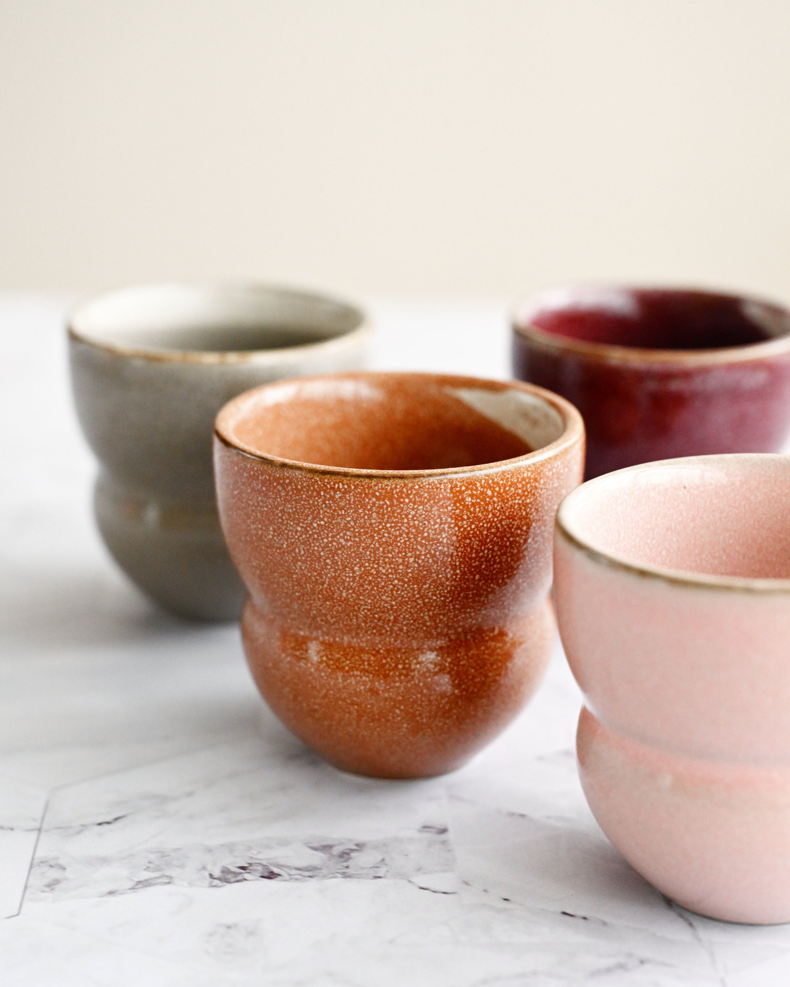 Four ceramic cups in different colors on a marble surface
