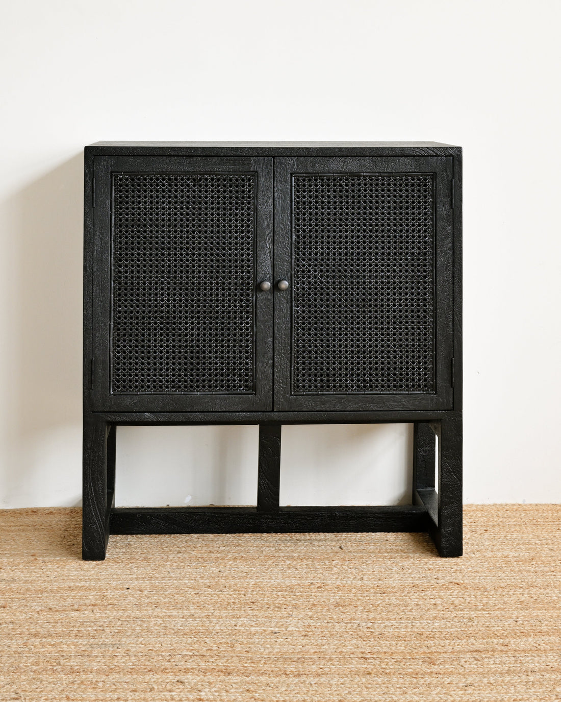 Black cabinet with woven design on a beige floor and white wall