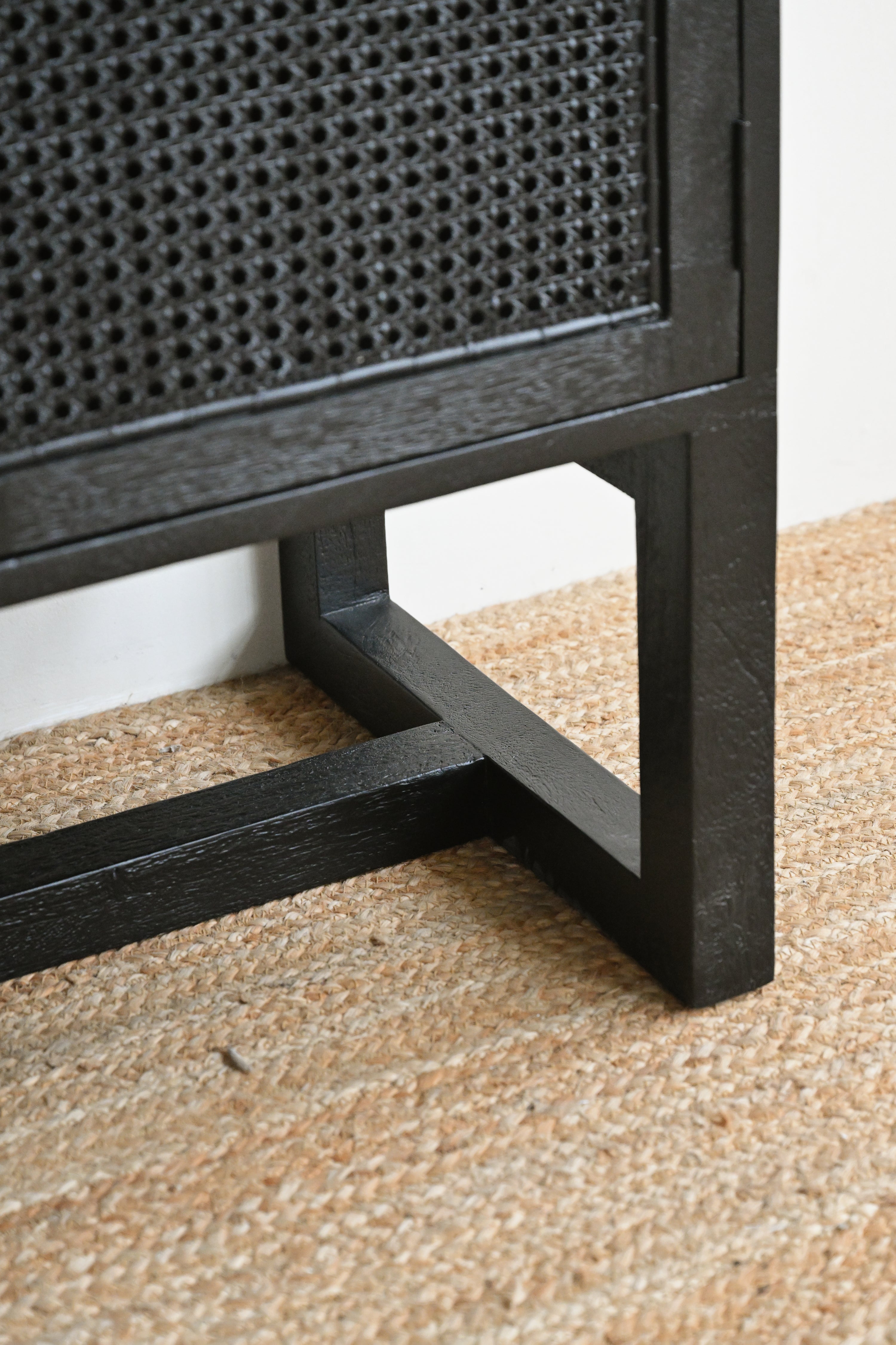 Close-up of a black rattan cabinet corner on a textured beige floor.