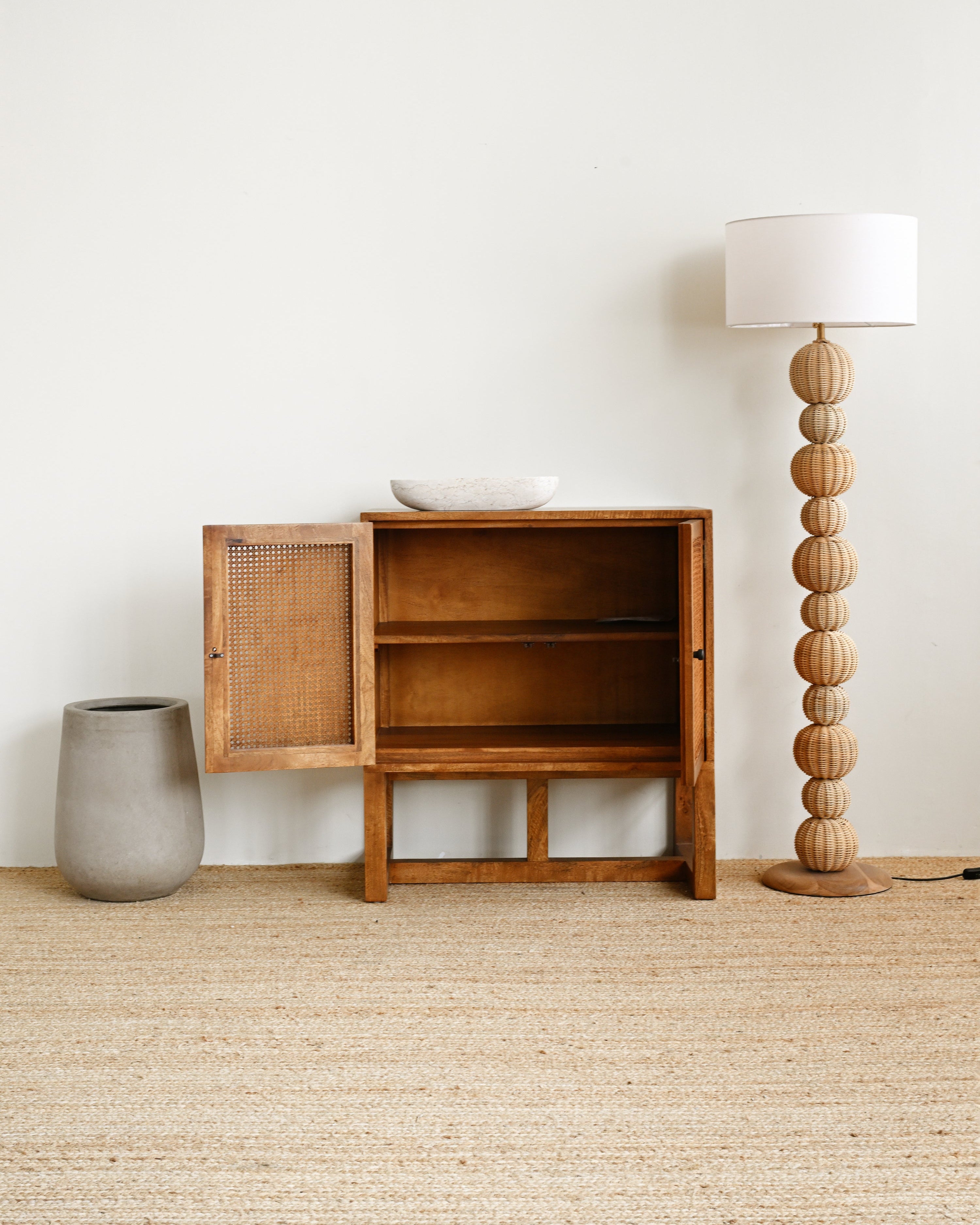 Wooden cabinet with open door on a beige carpet, next to a lamp and vase.
