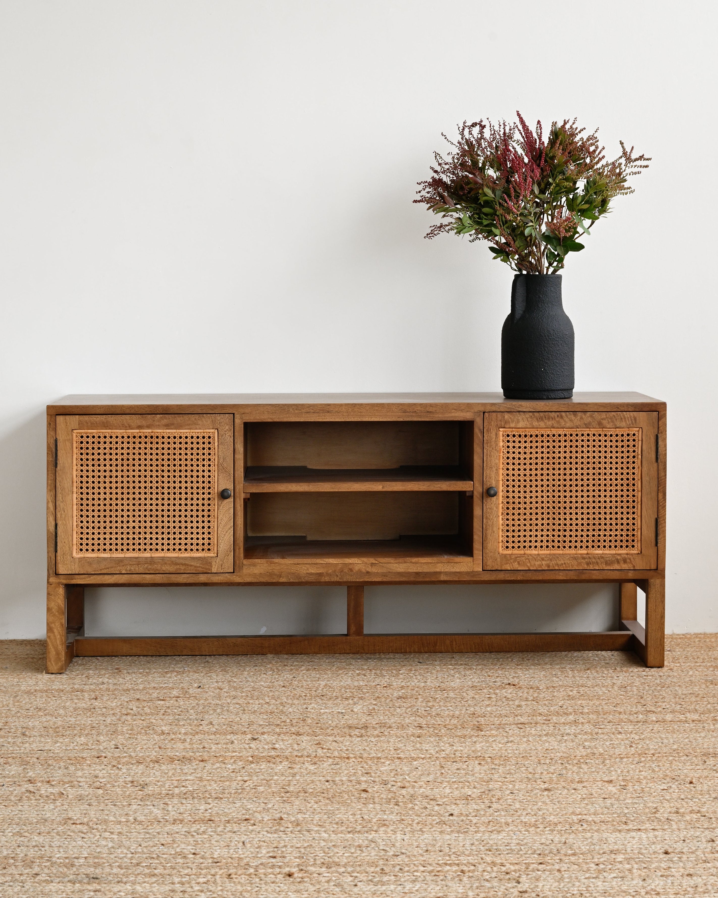 Wooden sideboard with rattan doors on a beige carpet against a white wall.