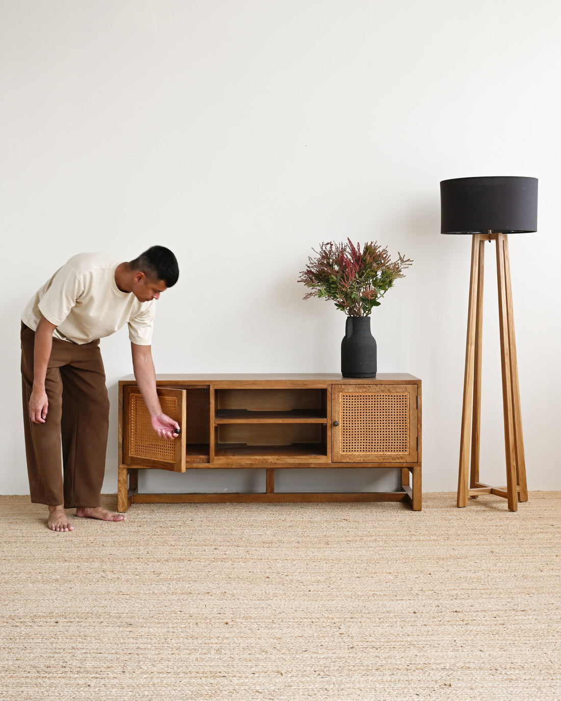 Person interacting with a wooden cabinet in a minimalistic room with a lamp and plant.
