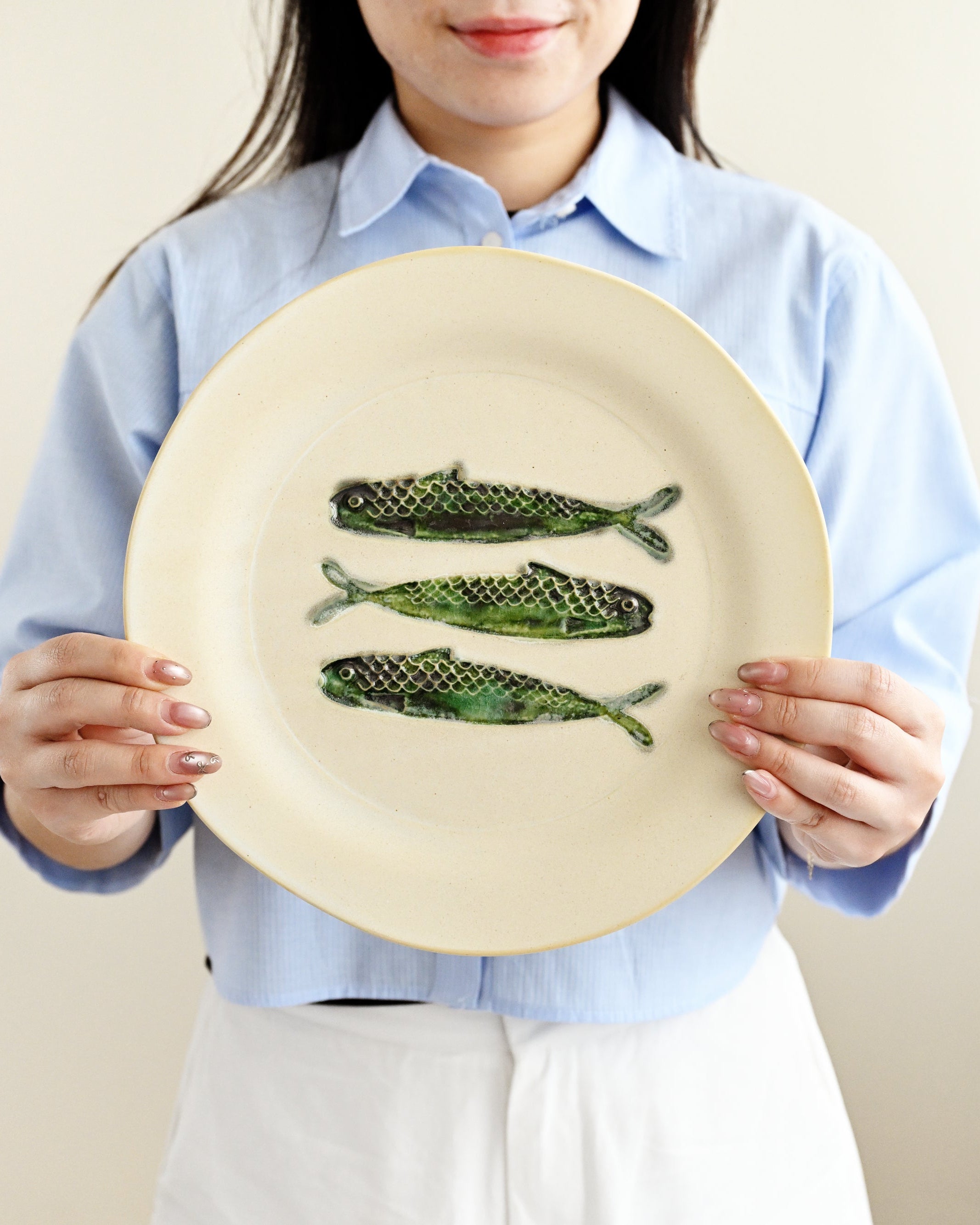 Person holding a plate with three fish illustrations against a plain background