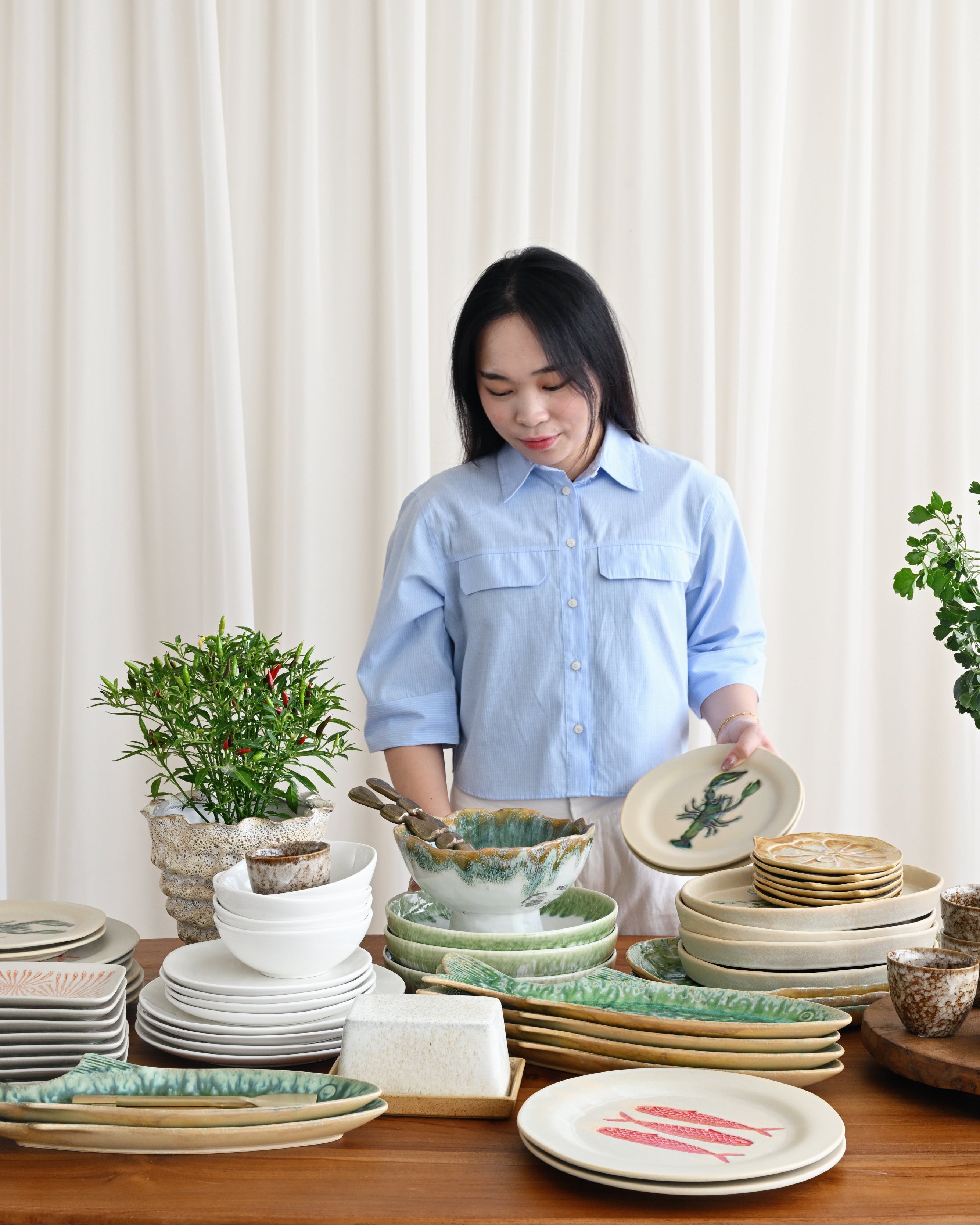 Woman in a light blue shirt standing behind a table with various ceramic plates and bowls.