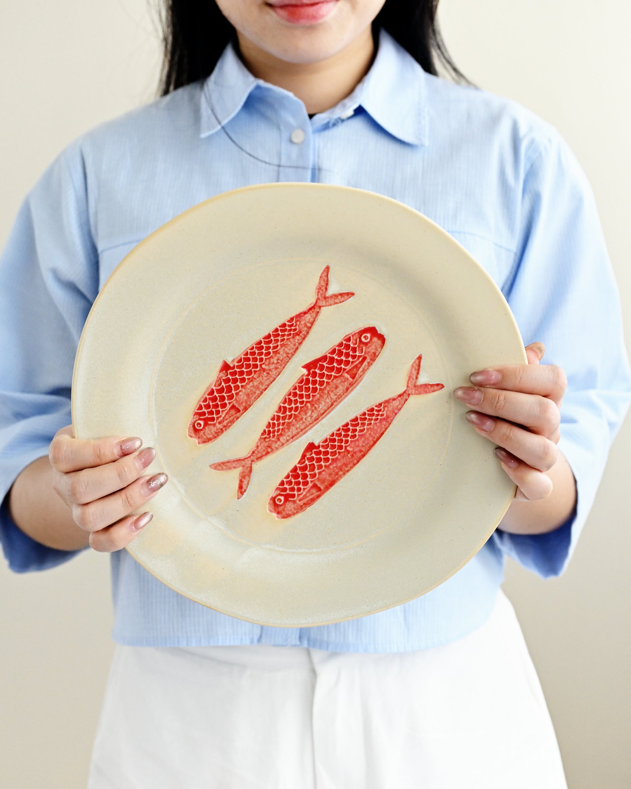 Person holding a plate with red fish illustrations against a plain background