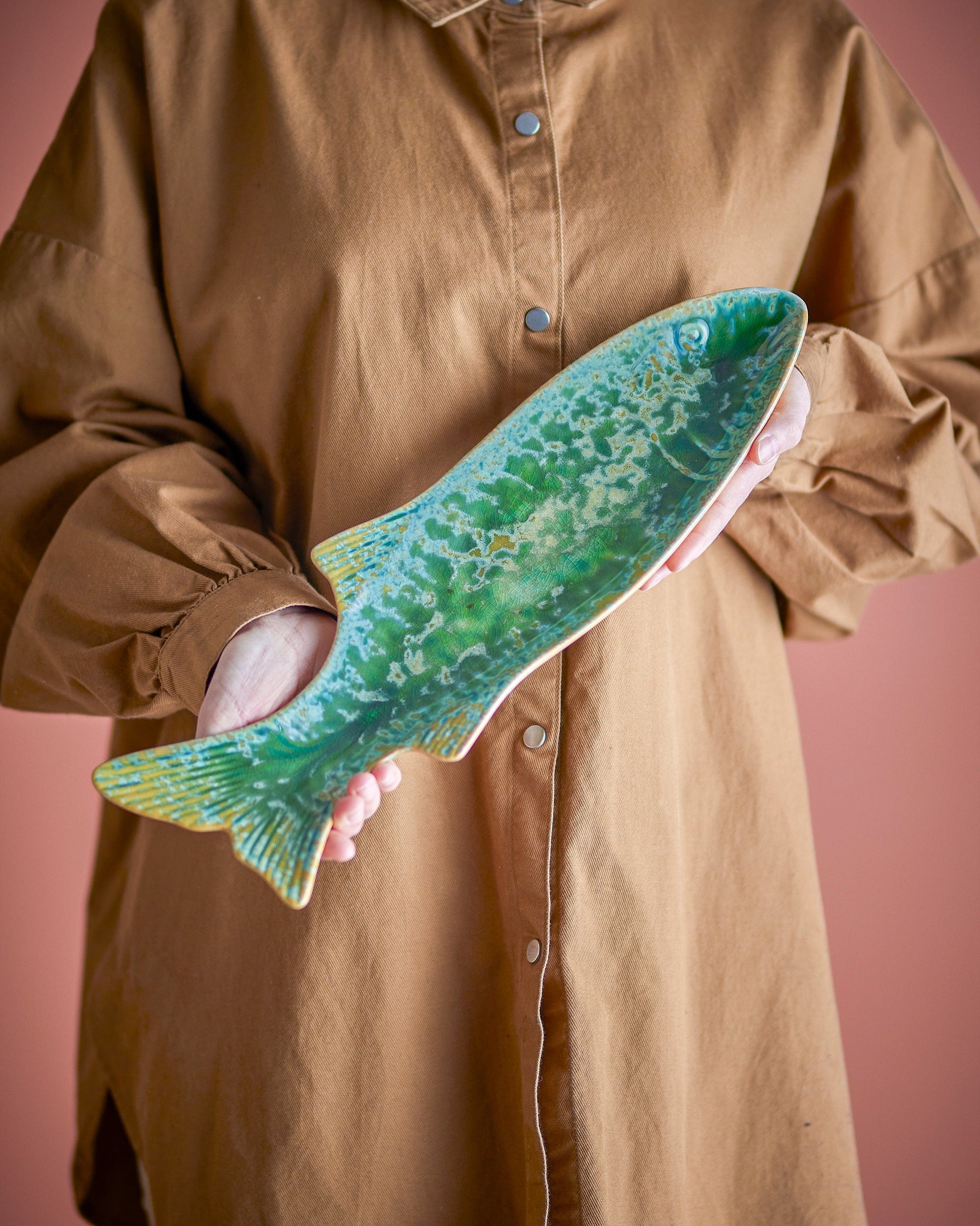Person holding a large green fish against a pink background
