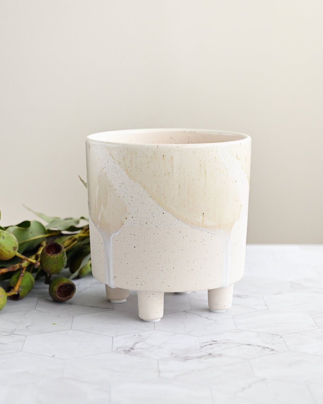 White ceramic planter with greenery on a light surface and beige background