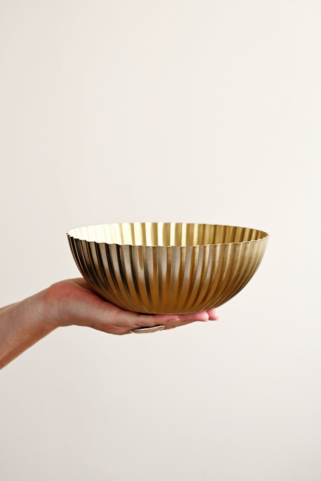 Hand holding a gold metallic bowl against a plain background