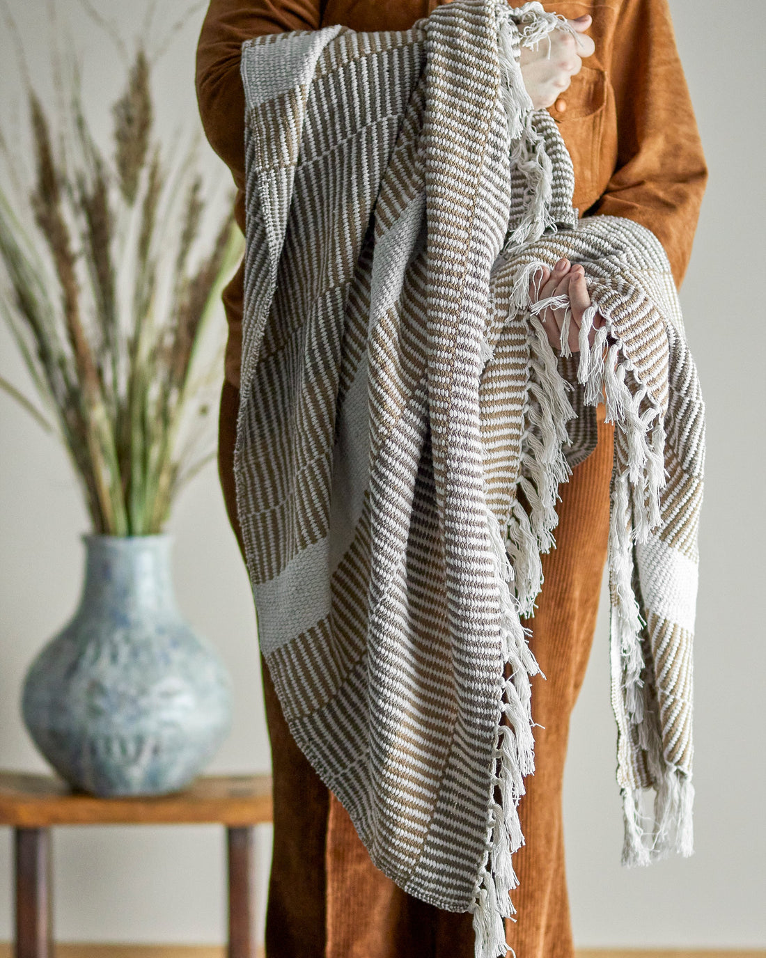 Person holding a textured blanket with a vase and plant in the background