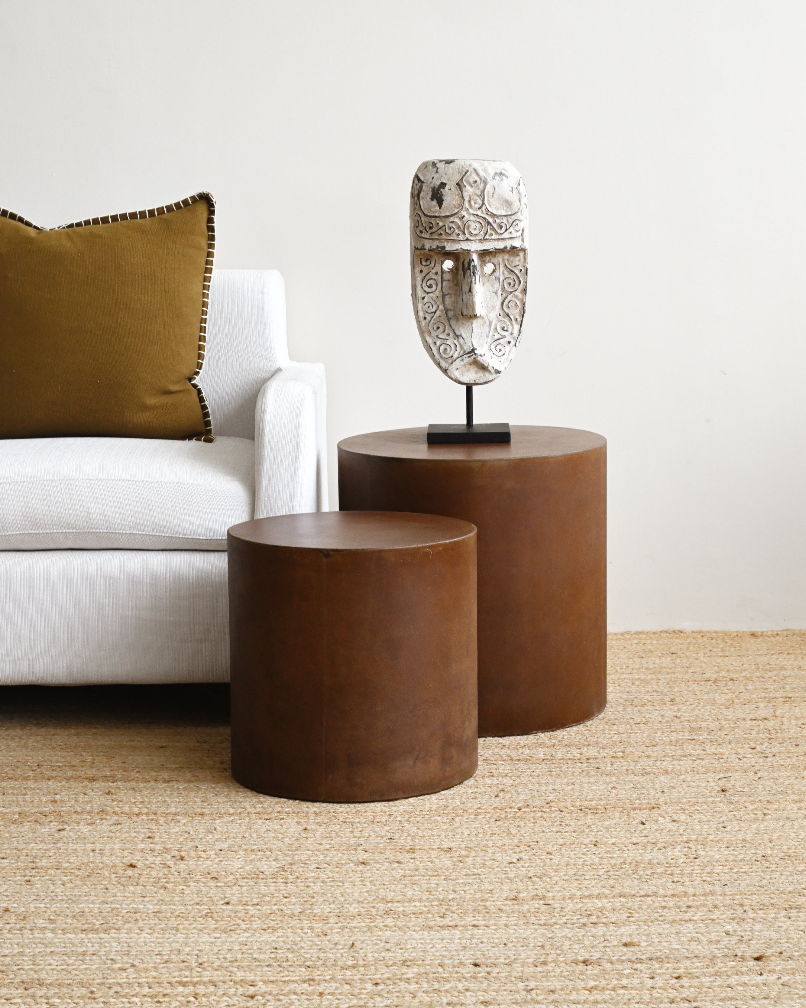 Two brown side tables with a decorative mask on a light-colored rug.