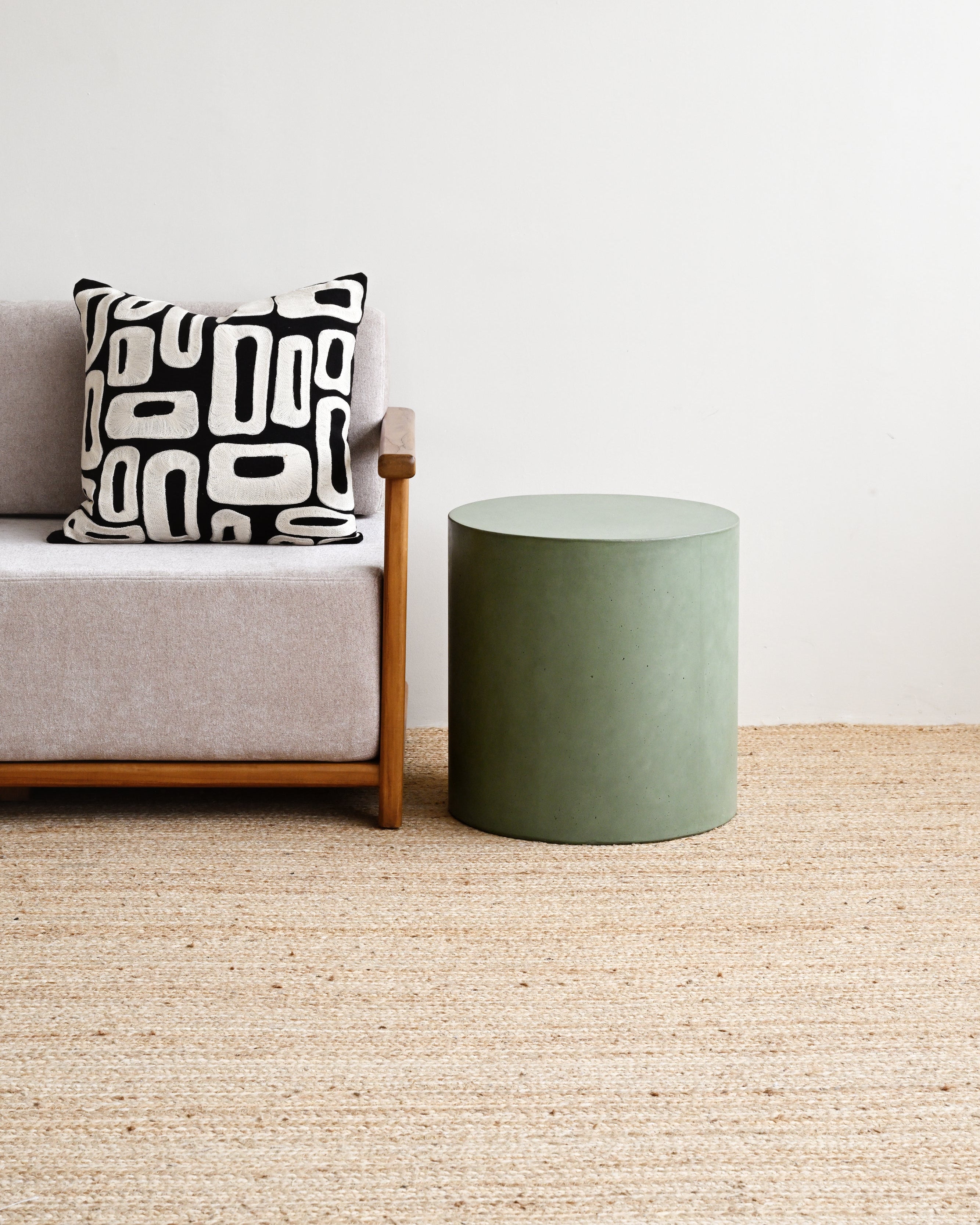 Gray sofa with a black and white patterned pillow next to a green cylindrical side table on a beige carpet.