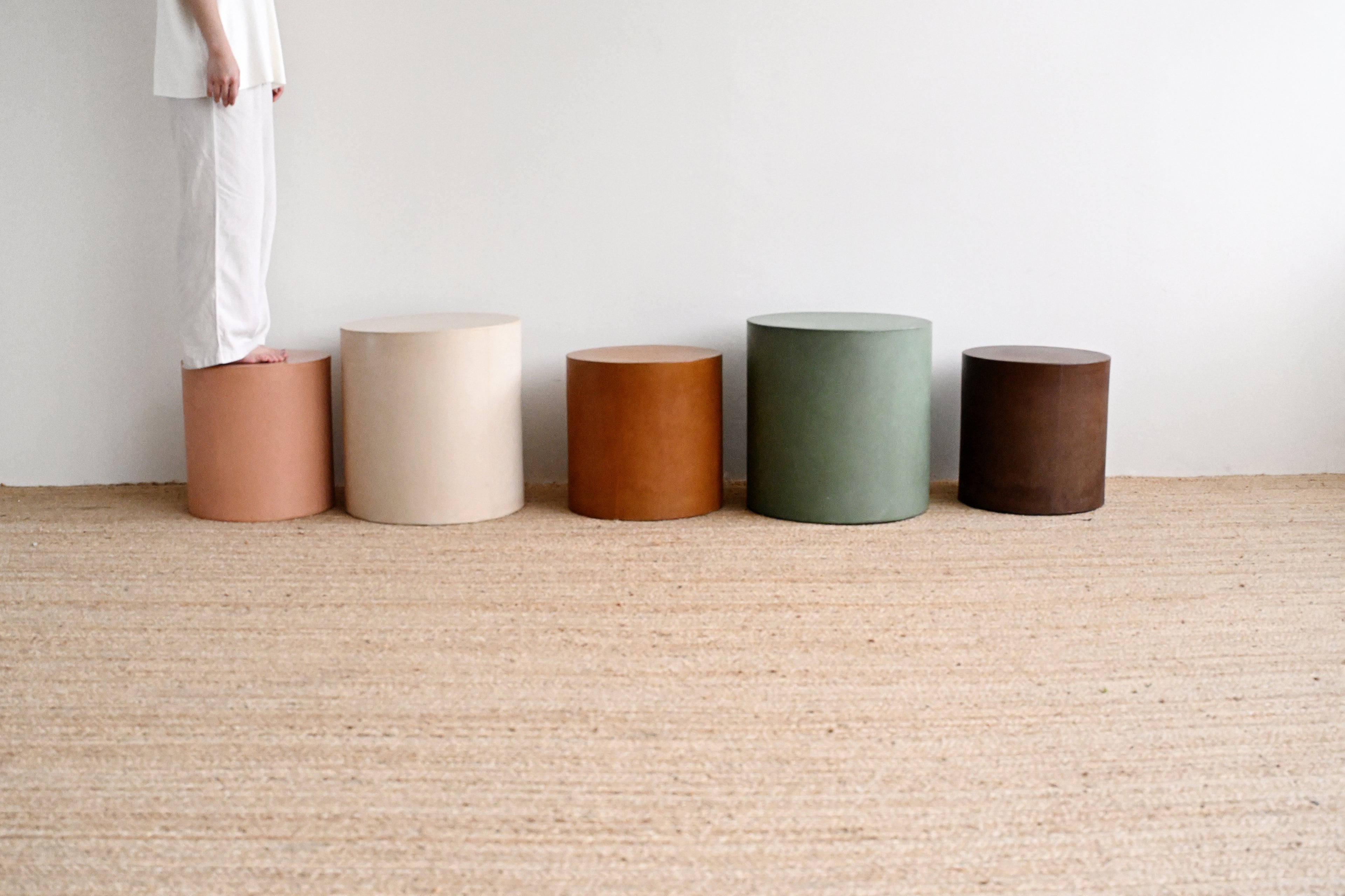 Five cylindrical stools in various colors arranged on a carpeted floor.