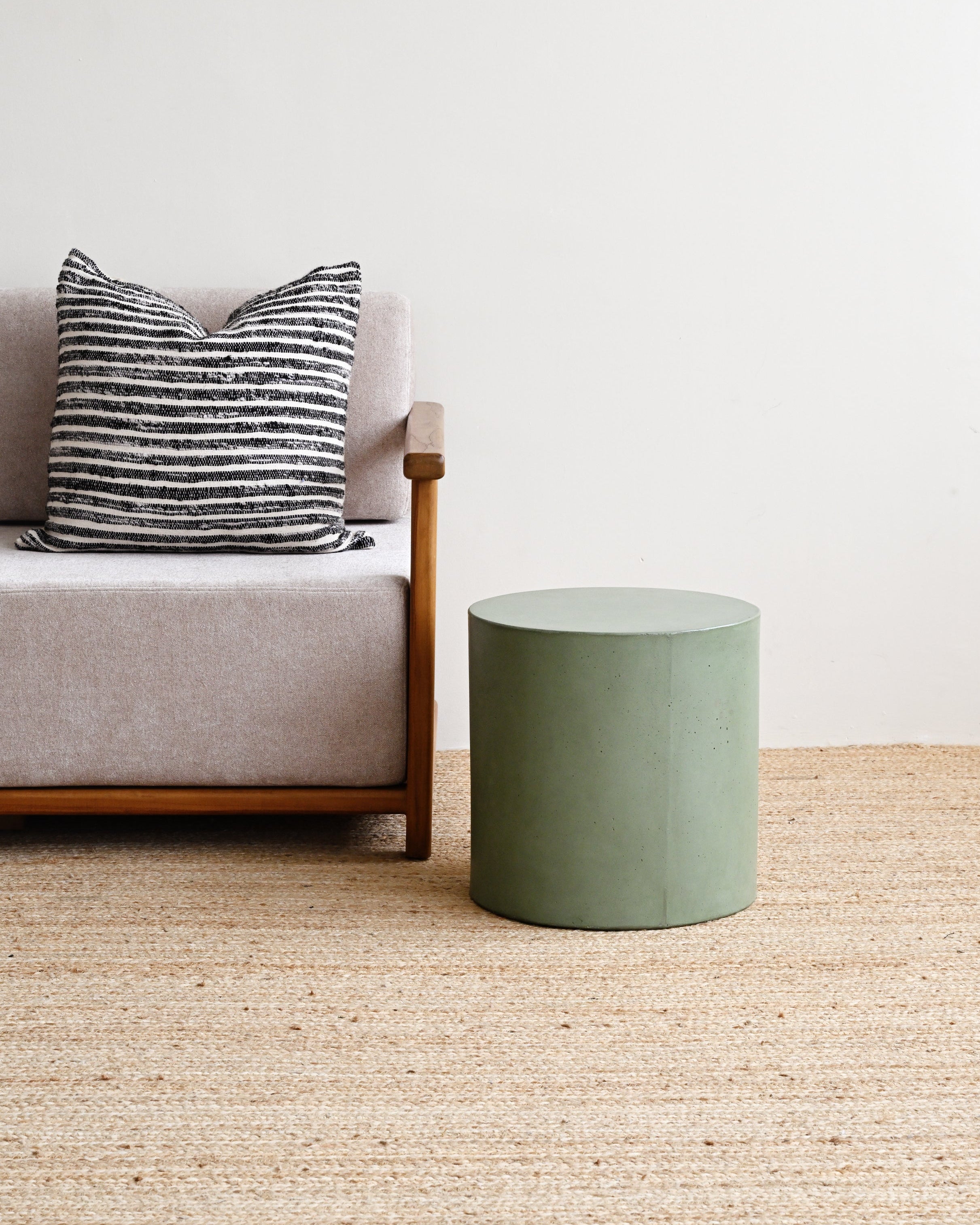 Green stool next to a gray sofa with a striped pillow on a beige carpet.