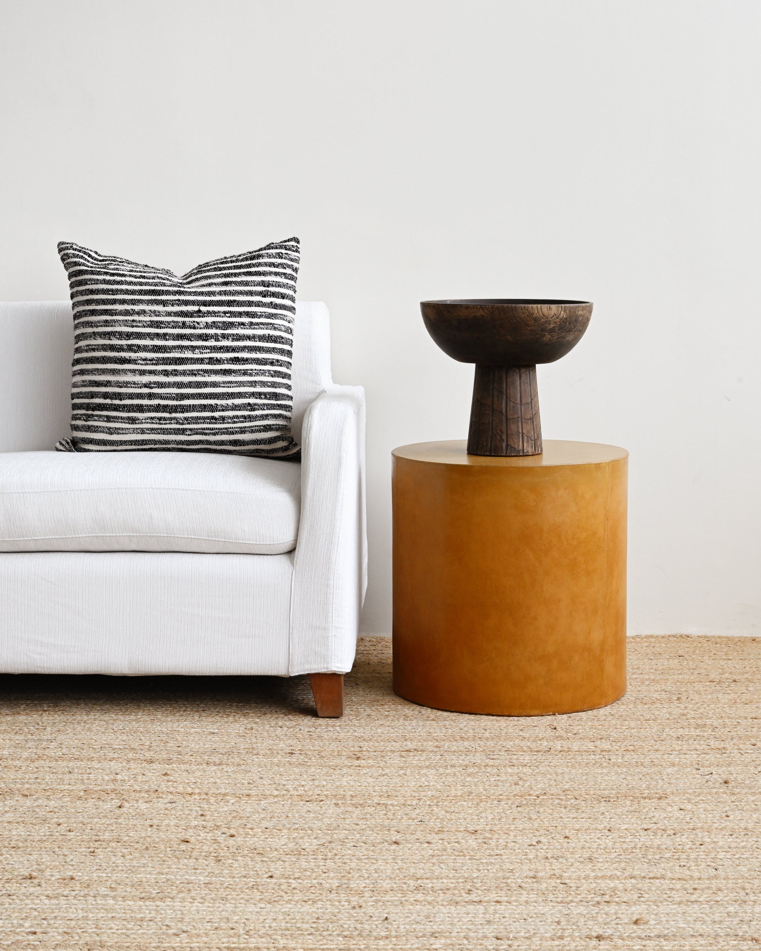 White sofa with a striped pillow and a brown side table in a minimalistic living room.