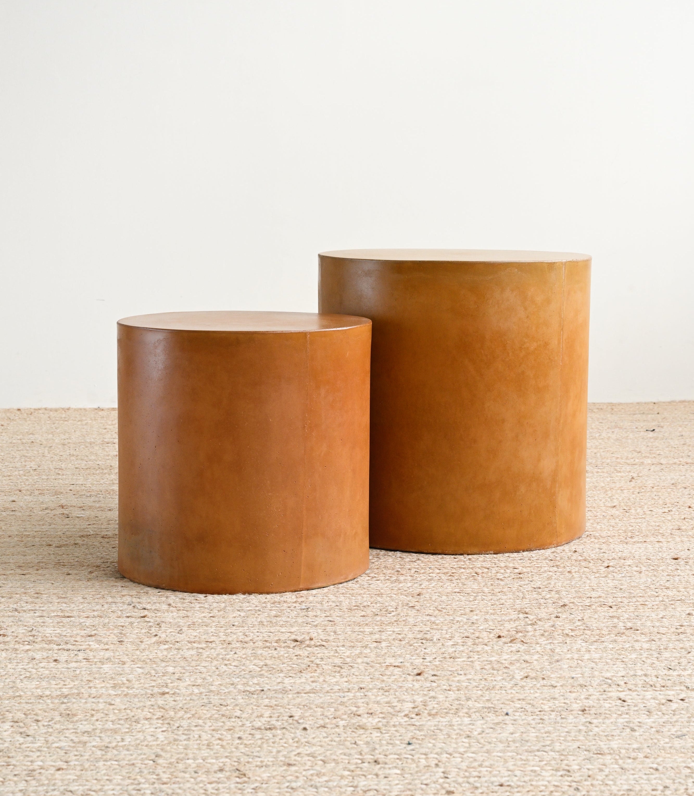 Two cylindrical leather ottomans on a textured surface with a neutral background